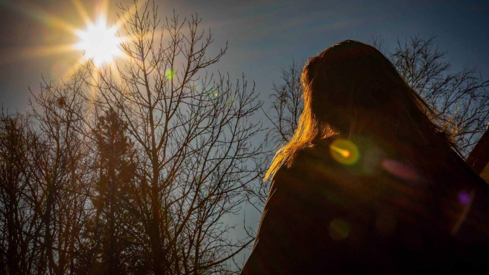 En kvinne står med ryggen til og kikker mot solen