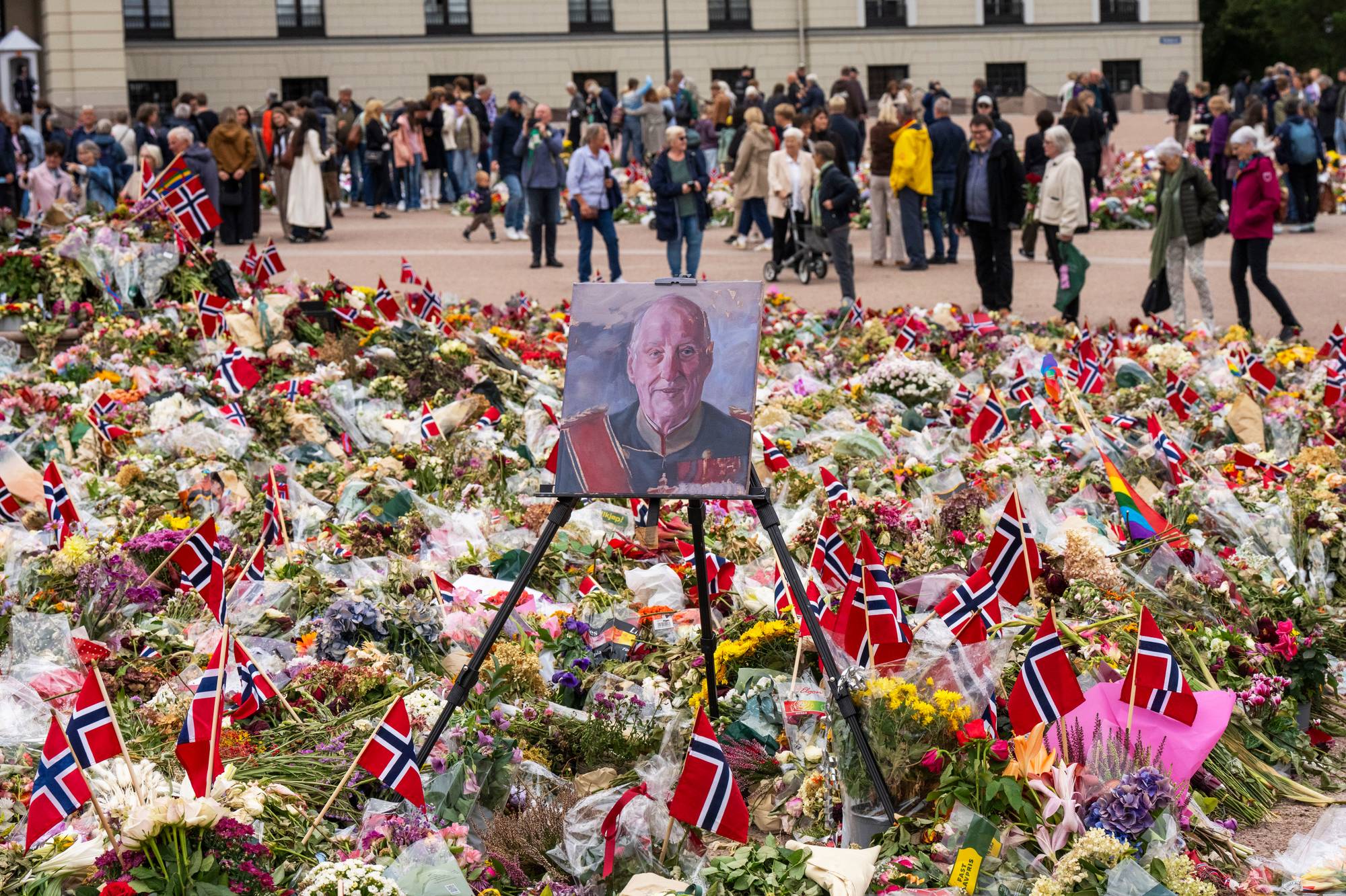 Et maleri av kong Harald står i blomsterhavet på Slottsplassen, i bakgrunnen sees mange mennesker