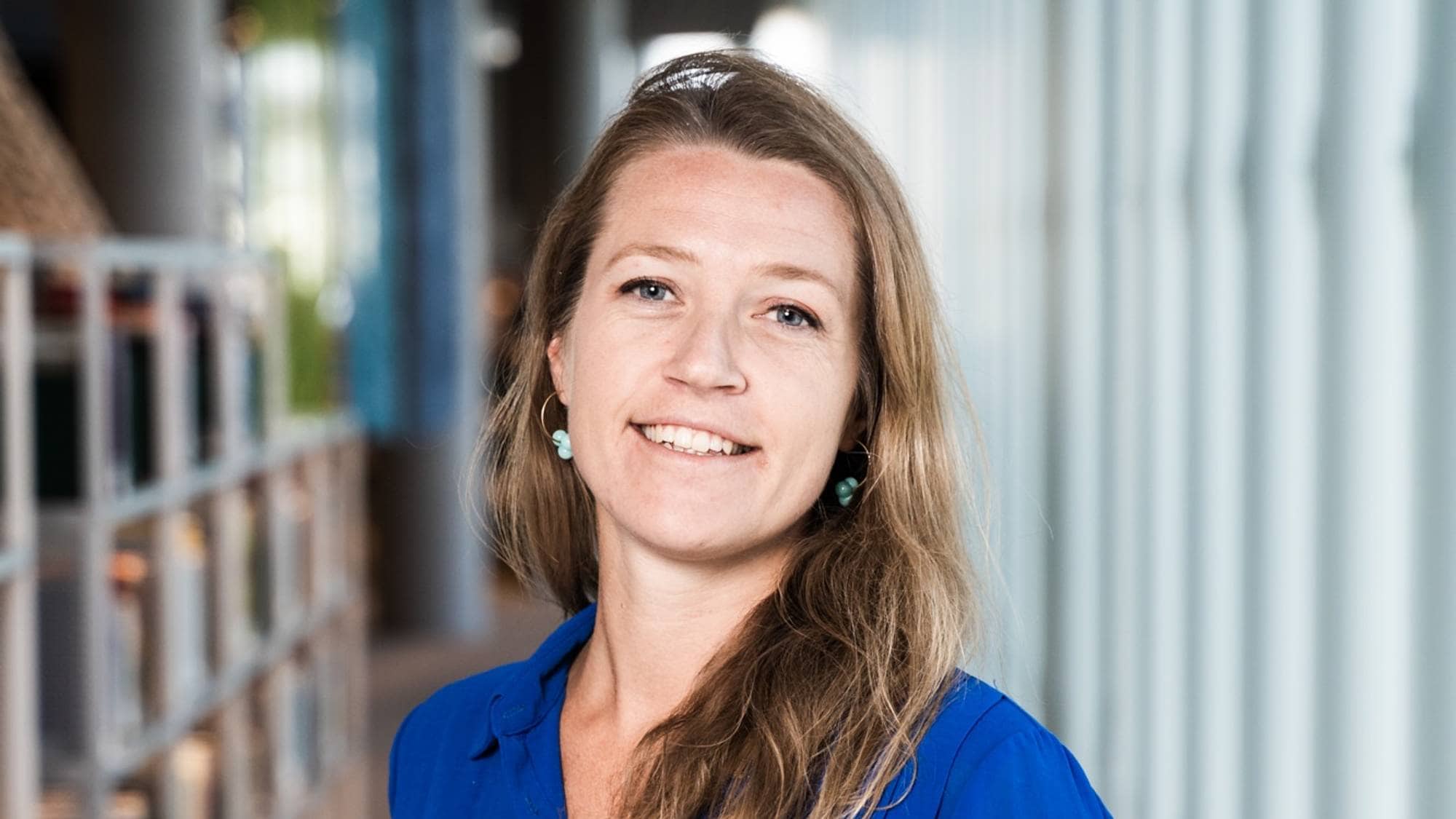 Helene Voldner står inne på et bibliotek foran mange bøker. 