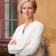 Actis Portrettbilde av generalsekretær Inger Lise Hansen i Actis i hvit skjorte foran en gul murvegg.