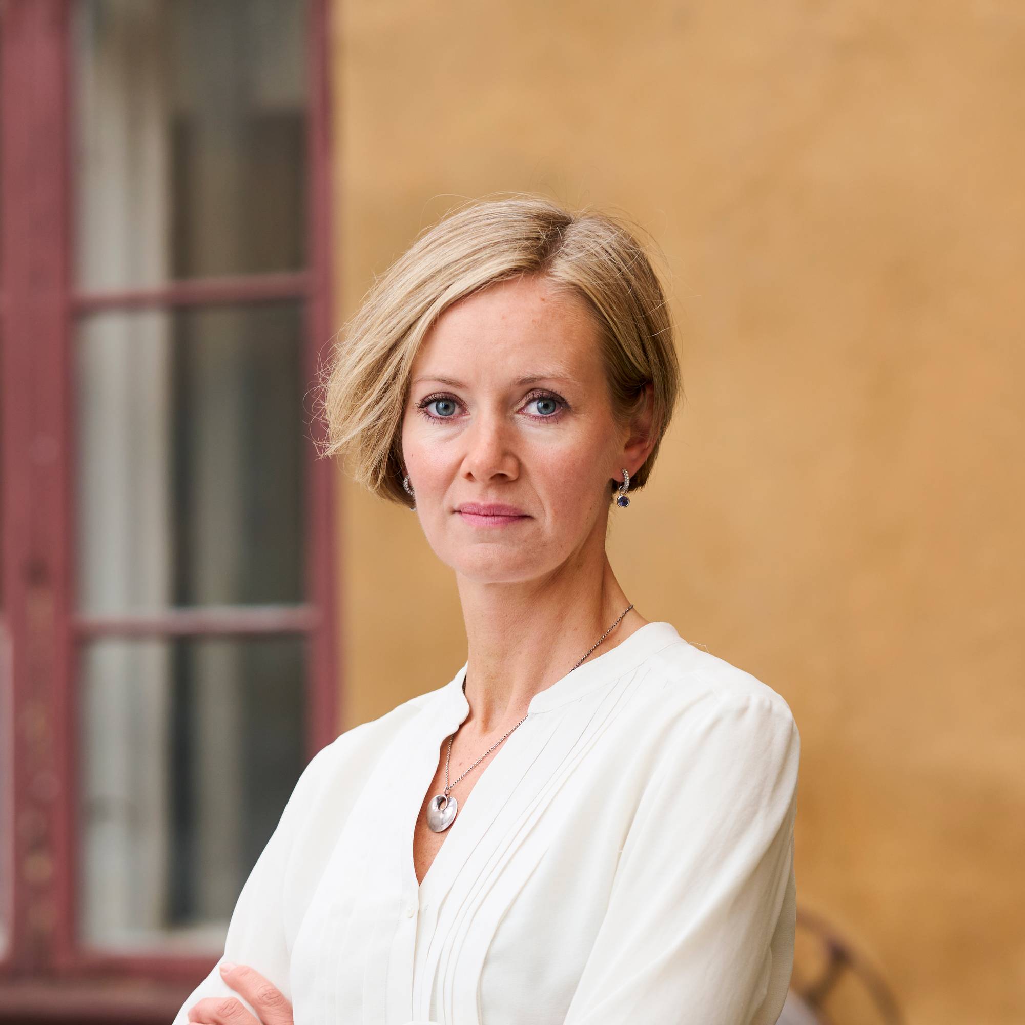 Portrettbilde av generalsekretær Inger Lise Hansen i Actis i hvit skjorte foran en gul murvegg. 
