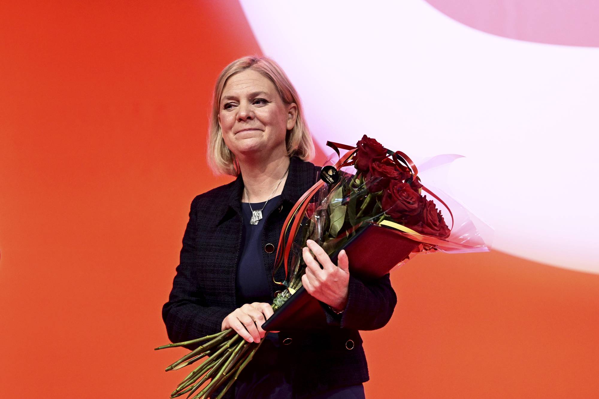 Magdalena Andersson holder en blomsterbukett foran en oransje bakgrunn. (Bildebeskrivelsen er laget av en KI-tjeneste)
