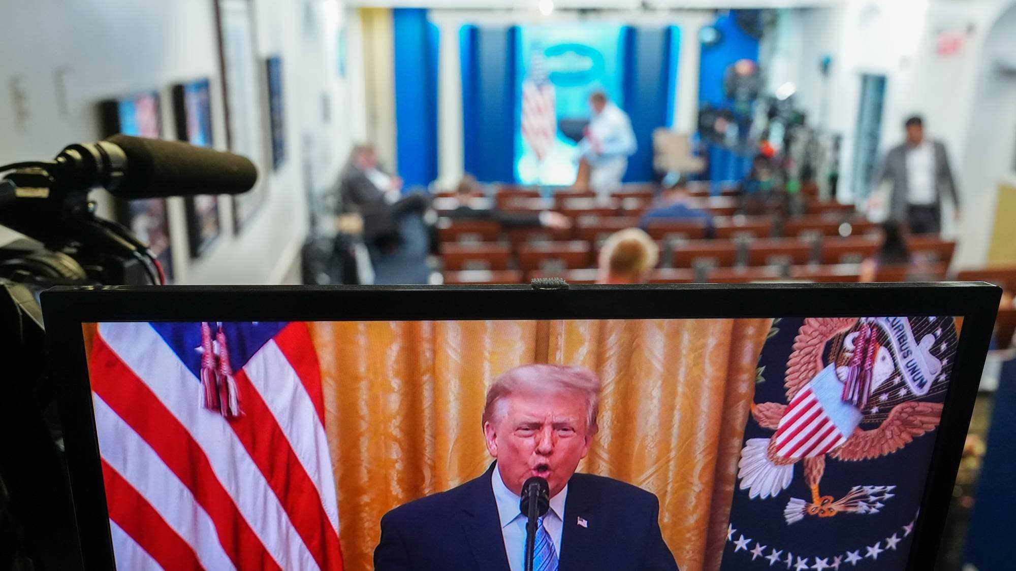 Donald Trump vises på en skjerm i et presserom med amerikanske flagg og riksvåpen i bakgrunnen. (Bildebeskrivelsen er laget av en KI-tjeneste)