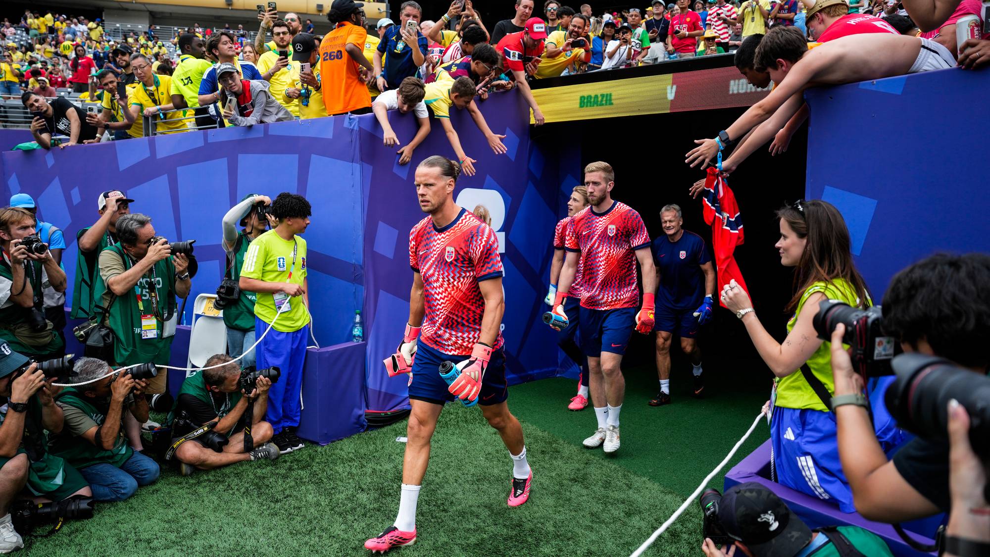 Norske fotballspillere går ut på banen omgitt av fotografer og publikum. (Bildebeskrivelsen er laget av en KI-tjeneste)