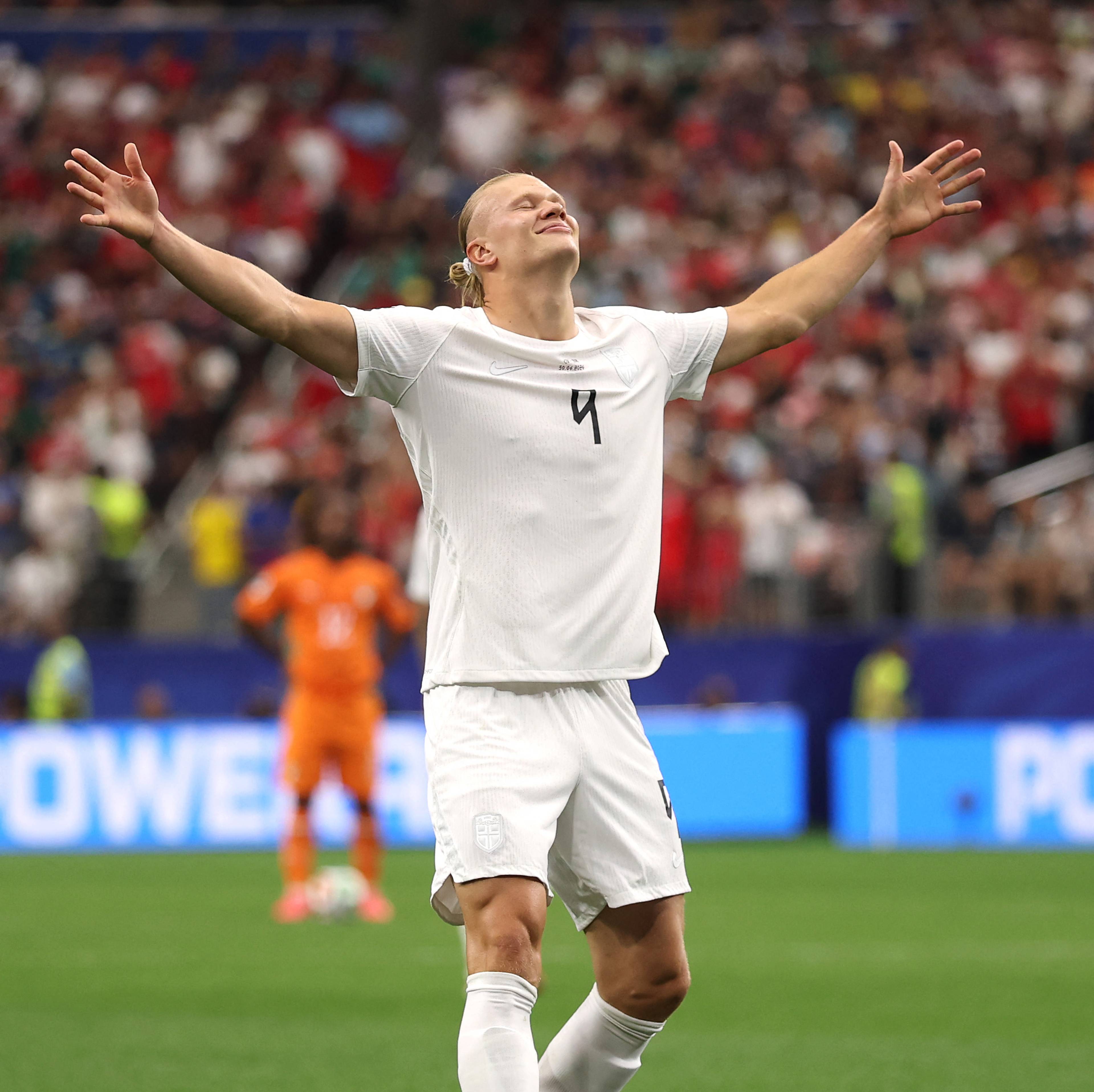 Erling Braut Haaland feirer med utstrakte armer på en fotballbane foran et fullsatt stadion. (Bildebeskrivelsen er laget av en KI-tjeneste)