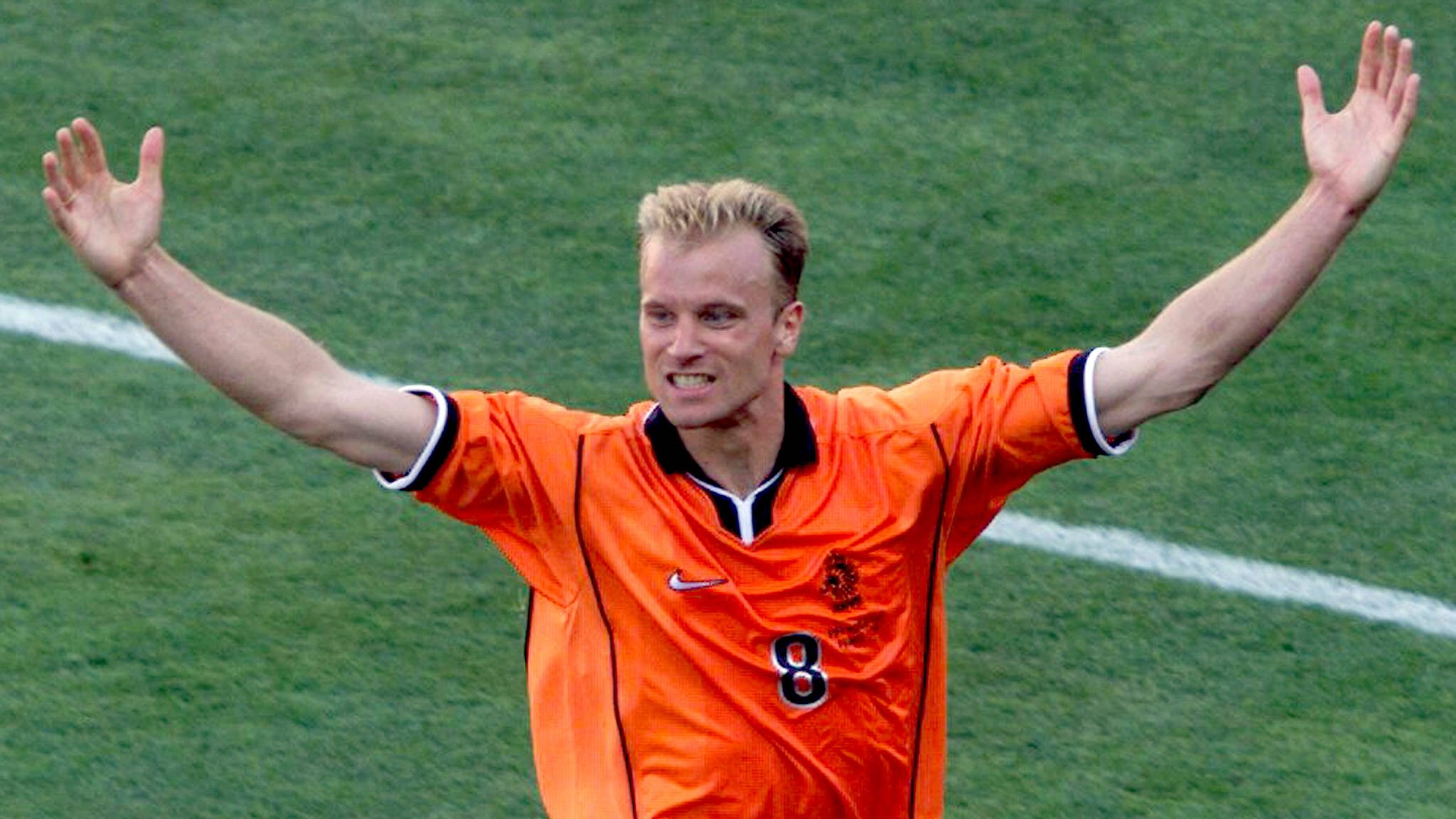 Dennis Bergkamp jubler med armene utstrakt på en fotballbane iført Nederland sin oransje landslagsdrakt. (Bildebeskrivelsen er laget av en KI-tjeneste)