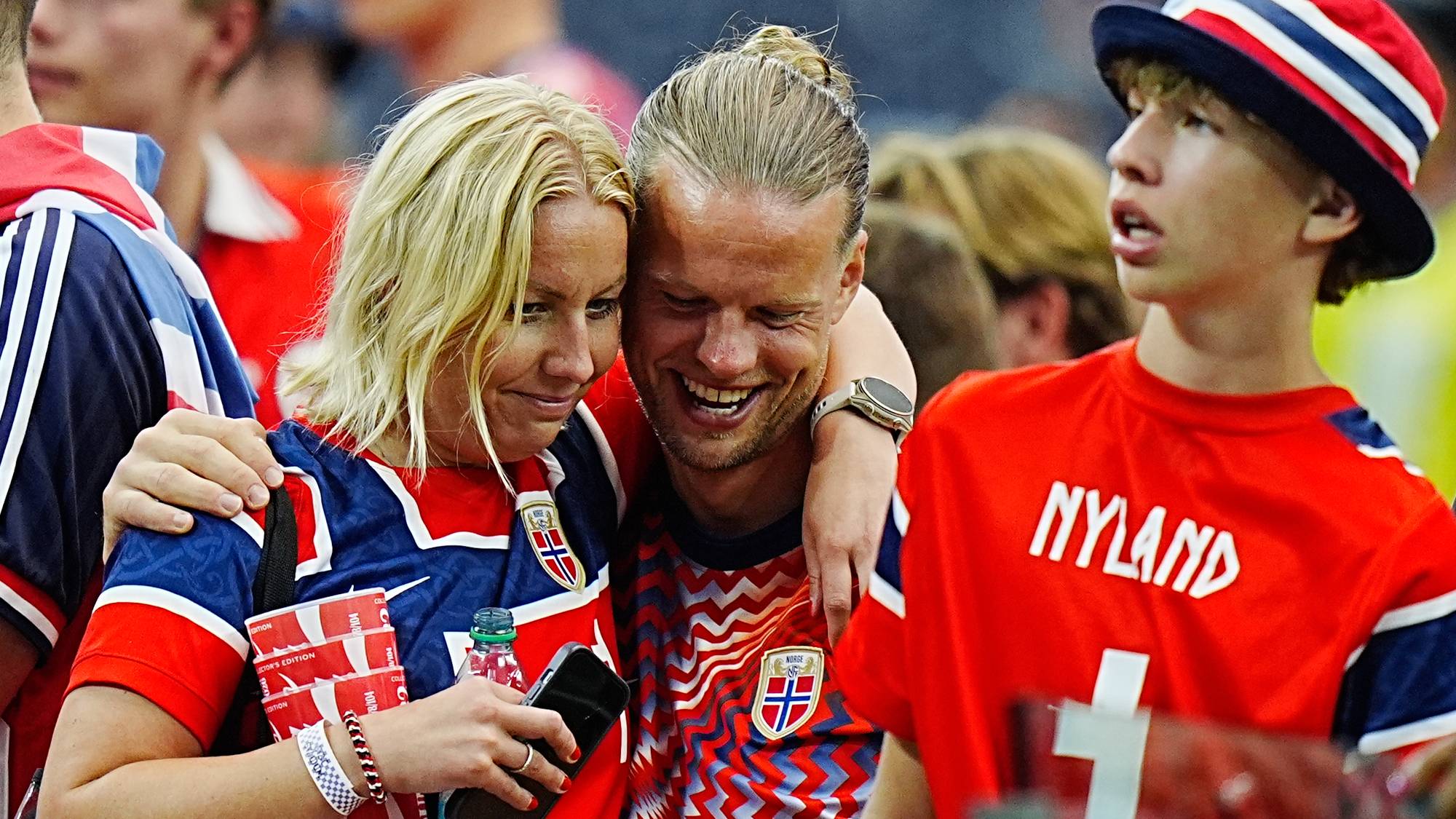 Fotballsupportere i norske landslagsdrakter står sammen på en tribune. (Bildebeskrivelsen er laget av en KI-tjeneste)
