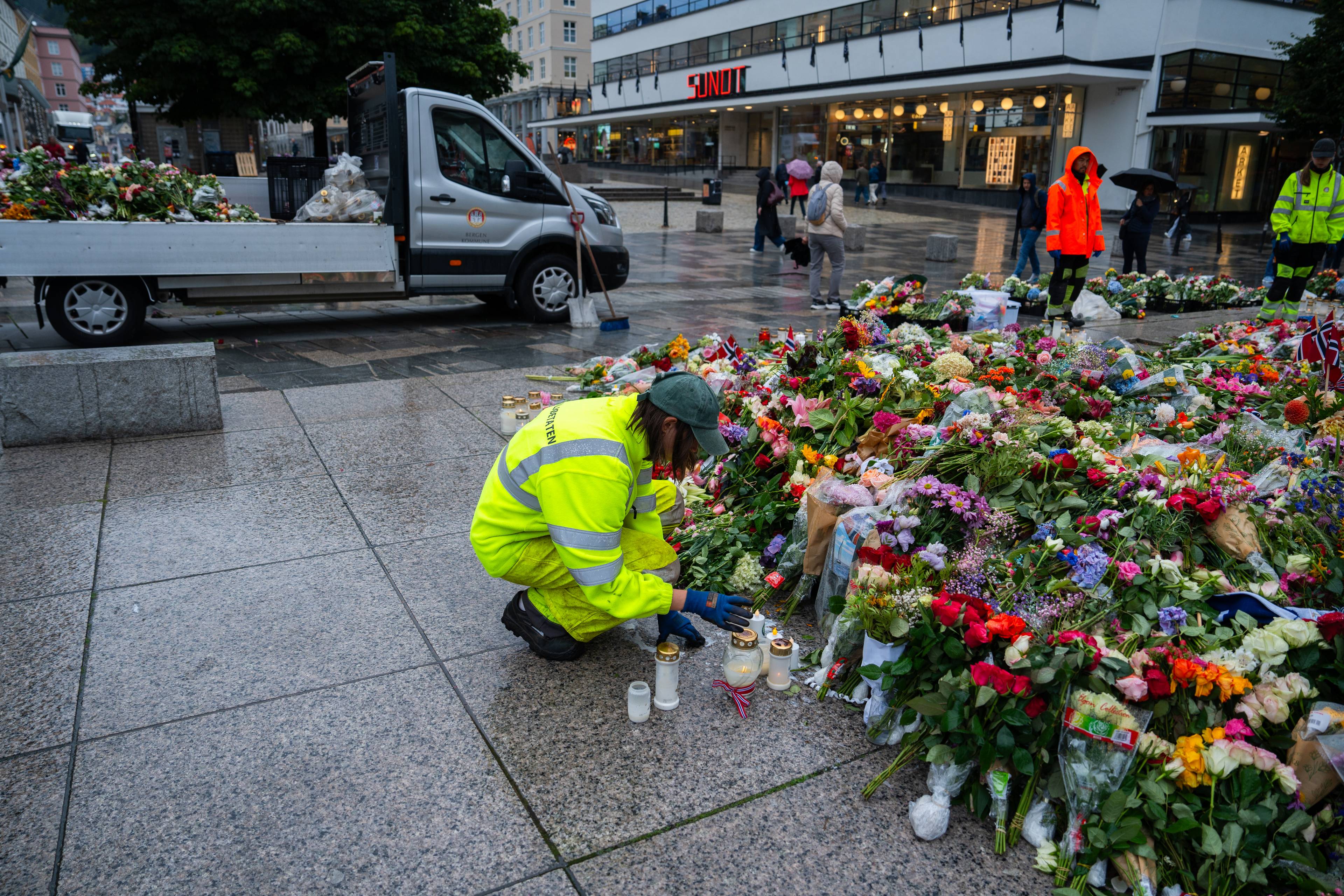 Mann i gule arbeidsklede ryddar i blomsterhavet rundt Den blå steinen i Bergen. Plukkar vekk rotne blomar, og set dei andre fint på plass.