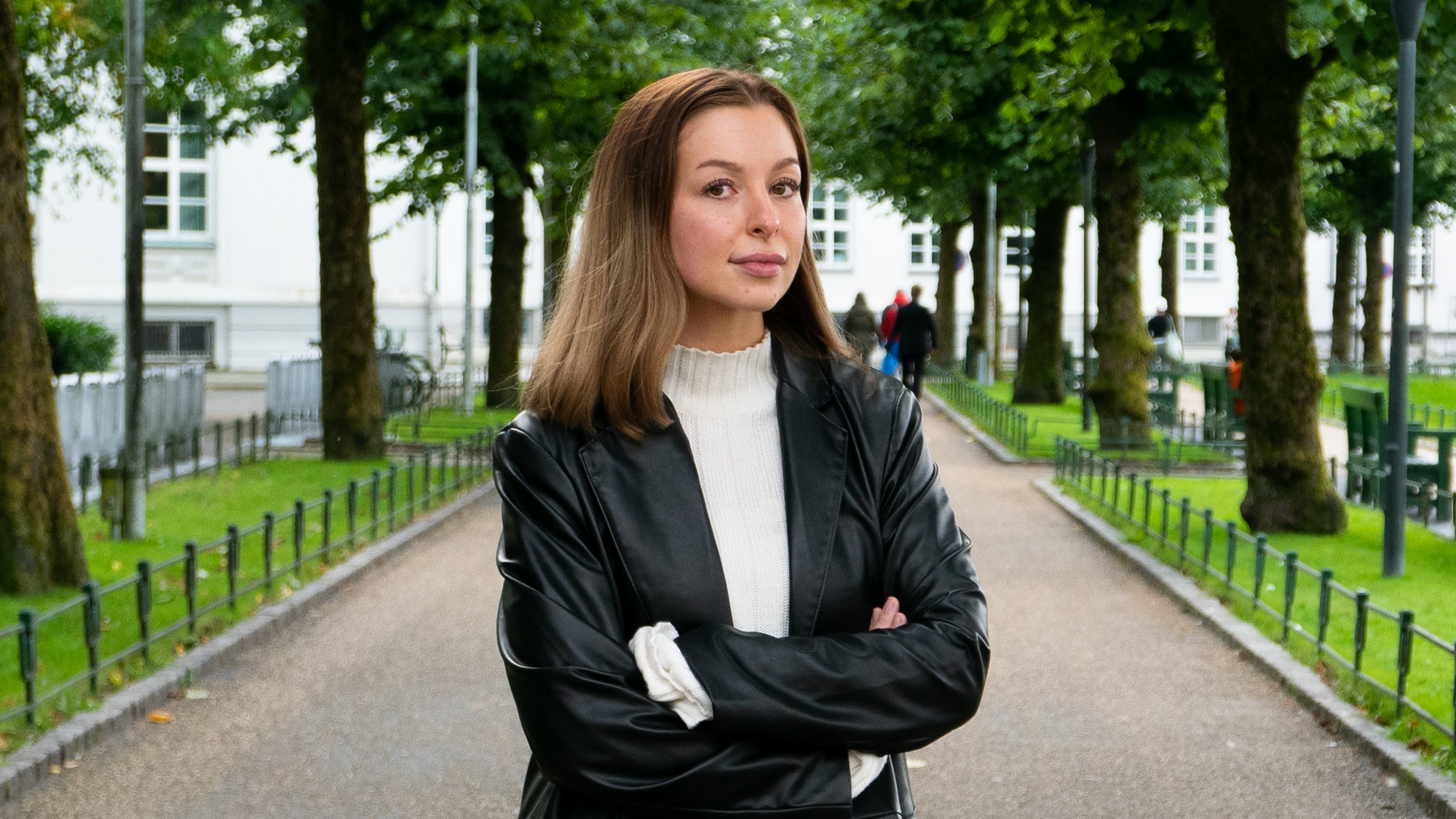 Skribenten står med armene i kryss i en frodig allé. Hun er ikledd en sort skinnjakke og hvit polo med et seriøst blikk mot kamera.