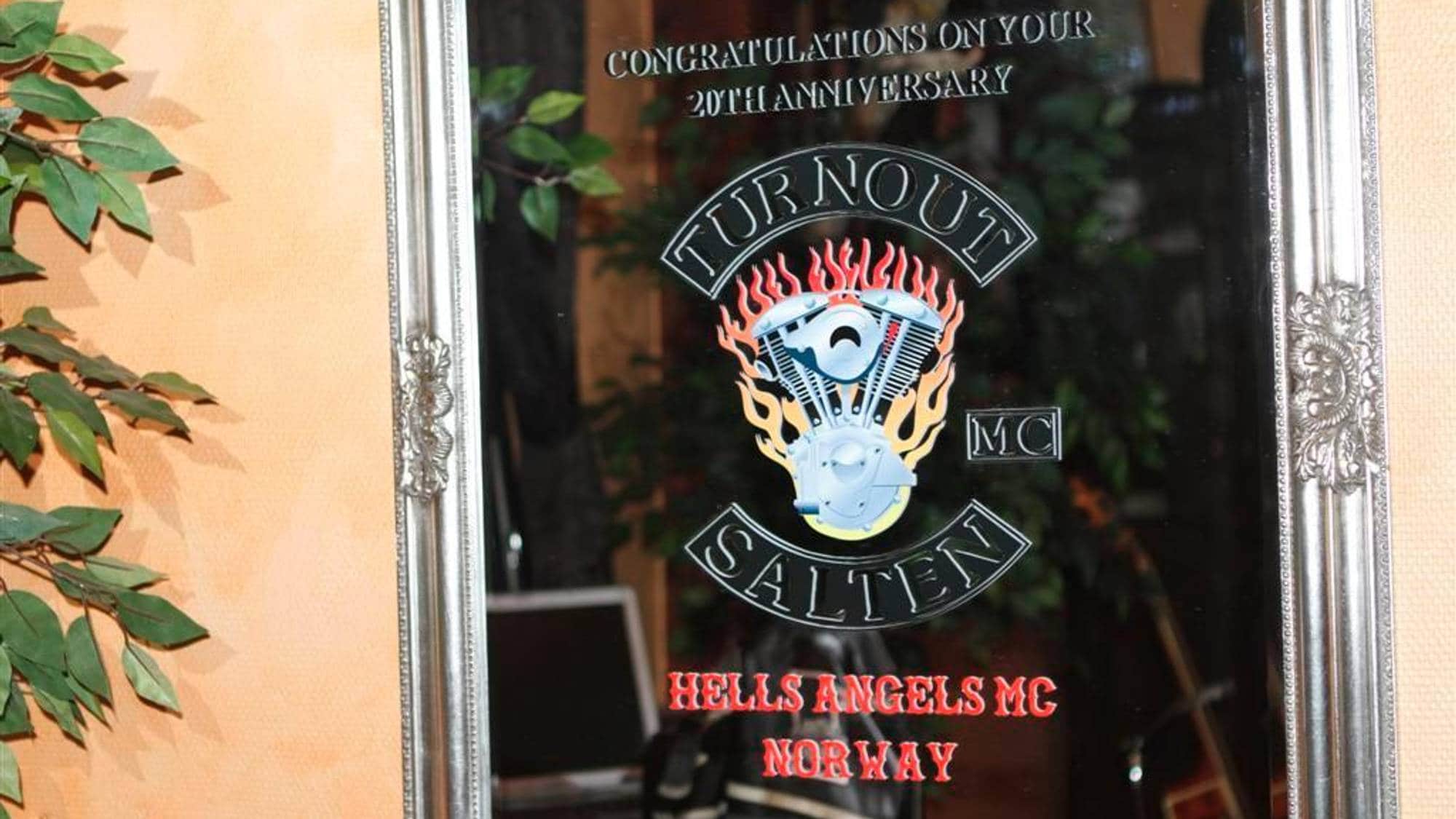 Speil med tekst og logo.
Teksten "CONGRATULATIONS ON YOUR 20TH ANNIVERSARY" og en logo med en motorsykkelmotor og flammer er synlig.
Under logoen står "TURN OUT SALTEN MC" og "HELLS ANGELS MC NORWAY".
Bildet viser et speil med dekorasjon. (Bildebeskrivelsen er laget av en KI-tjeneste)