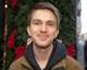 en mann som smiler til kameraet. Brunt hår og blå øyne. Bak han er julefargene grønn og rød.