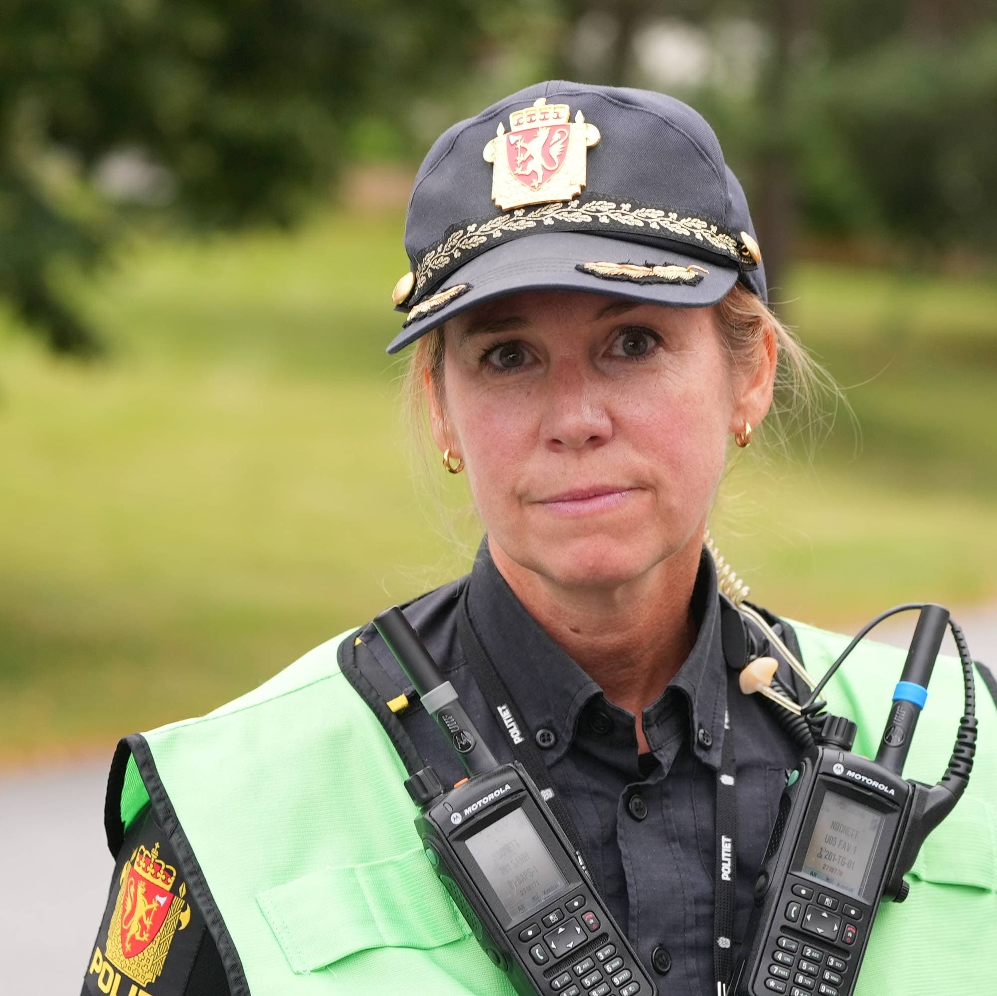 Kvinnelig politibetjent i uniform med gul refleksvest og samband utendørs. (Bildebeskrivelsen er laget av en KI-tjeneste)