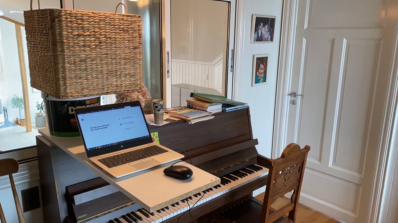 Hjemmekontor. For å få ståbord har han stablet en bordplate oppå et piano. Et malingsspann og en stor kurv er motvekt til PC og mus.