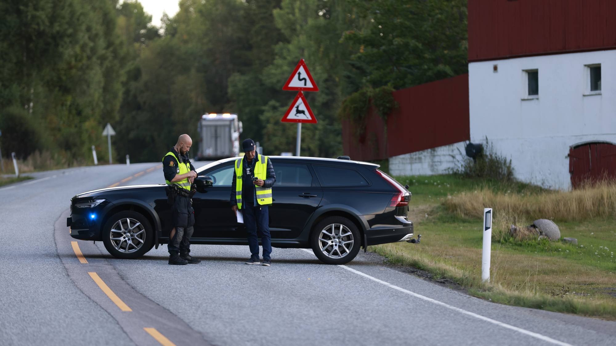 To menn med gule refleksvester foran en svart sivil politibil 