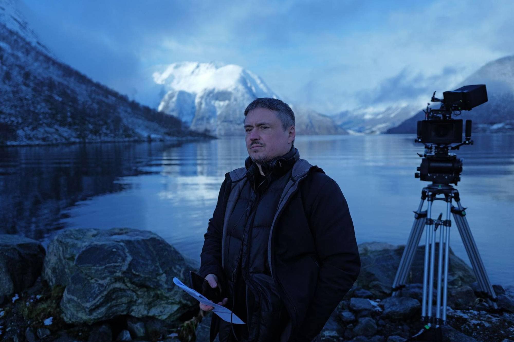 En mann som står foran et kamera ved en fjord.