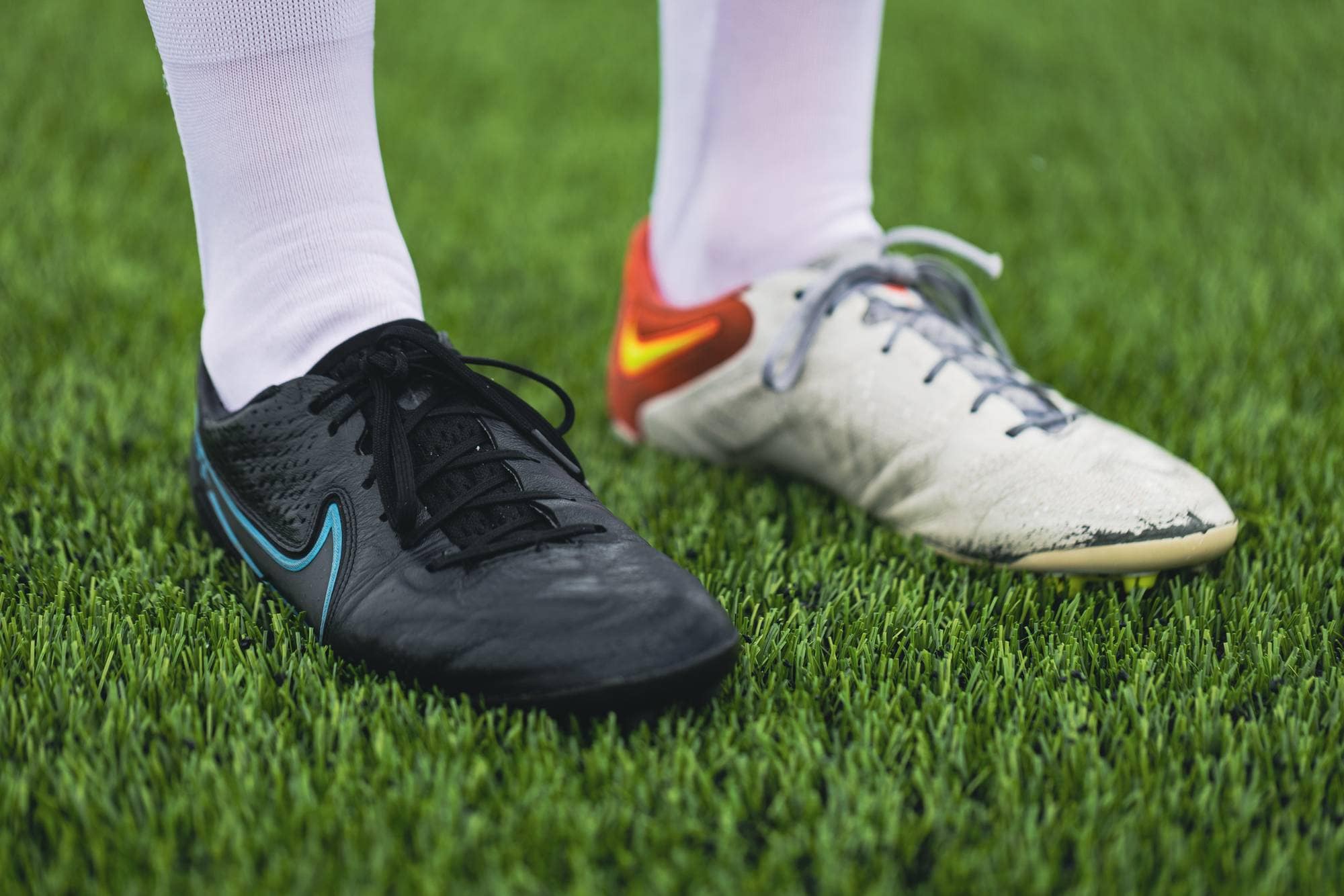 Et bilde av fotballskoene til Karina på det grønne kunstgresset. Hun har én sort og én hvit sko, men begge er av merket Nike og ser ut til å være samme modell.