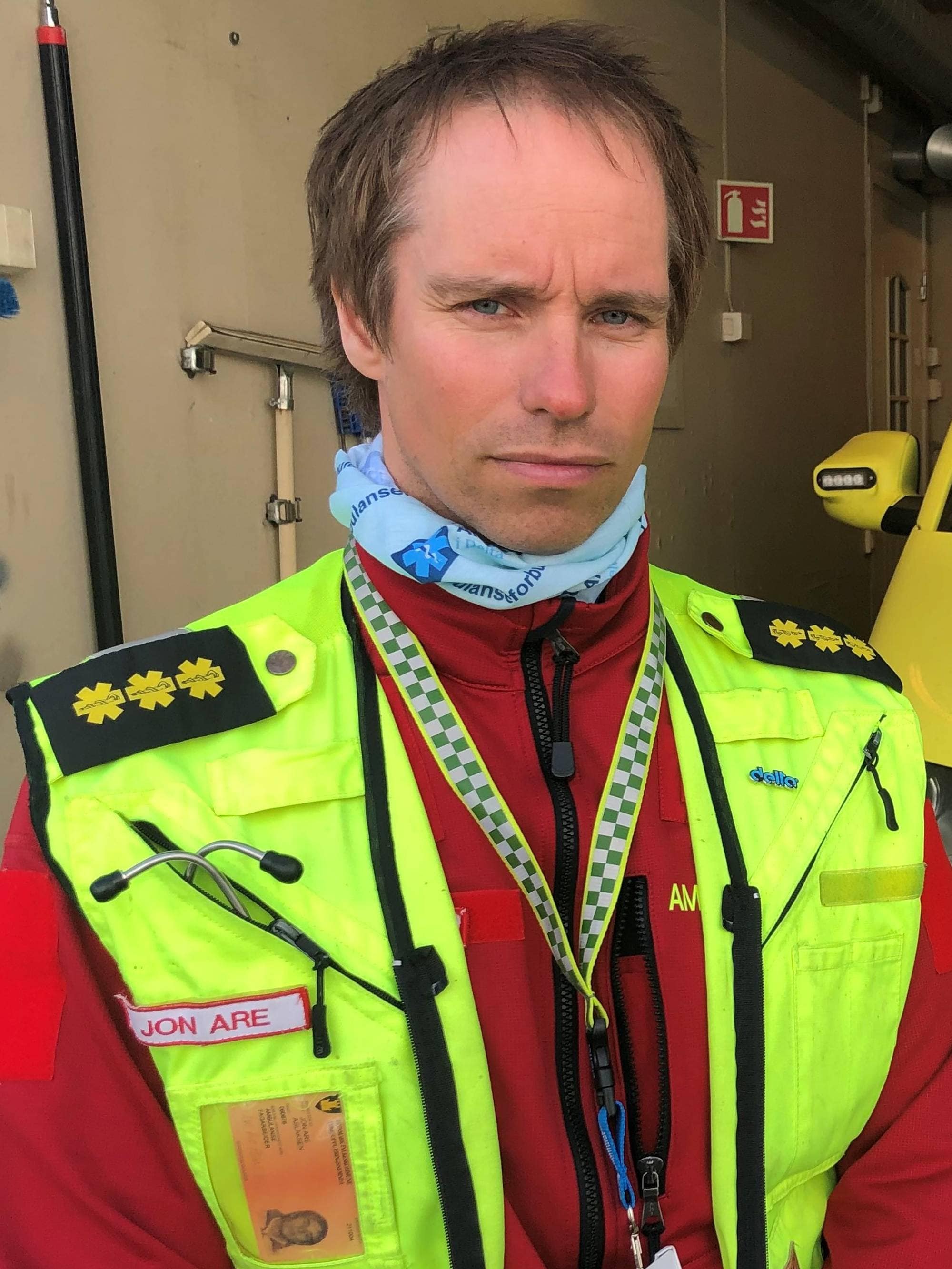 Ambulansepersonell foran en ambulanse i en garasje. (Bildebeskrivelsen er laget av en KI-tjeneste)