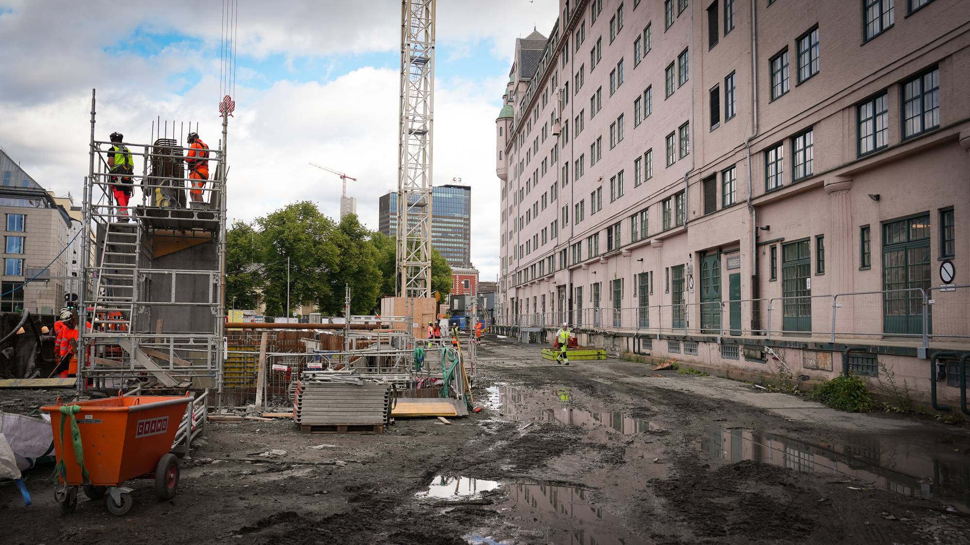 Arbeidere ved et byggeprosjekt i Oslo med en stor kran og bygårder i bakgrunnen. 