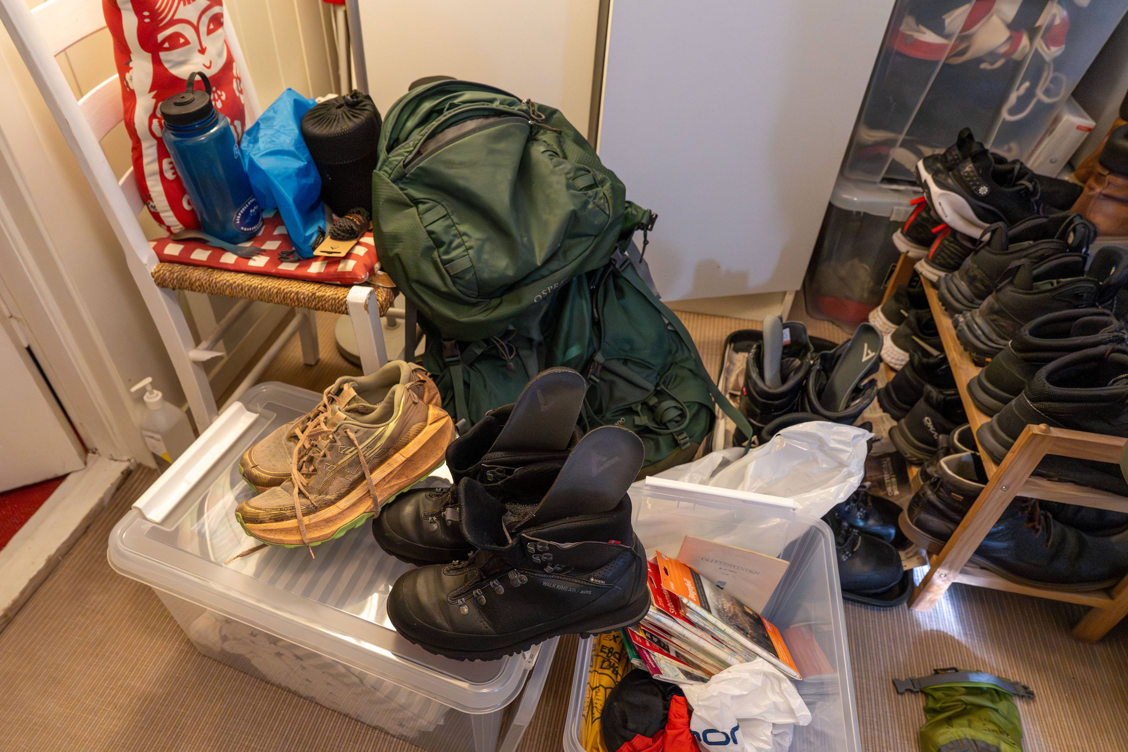 Turutstyr som sekk, fjellsko og plastkasser med utstyr er plassert på et gulv. (Bildebeskrivelsen er laget av en KI-tjeneste)