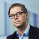 Handelsbanken / BÃ¥rd Gudim En mann med sleik, briller og noen få skjeggstubber ser inn i kameraet. Han har på seg en stripete, blå skjorte og dressjakke.