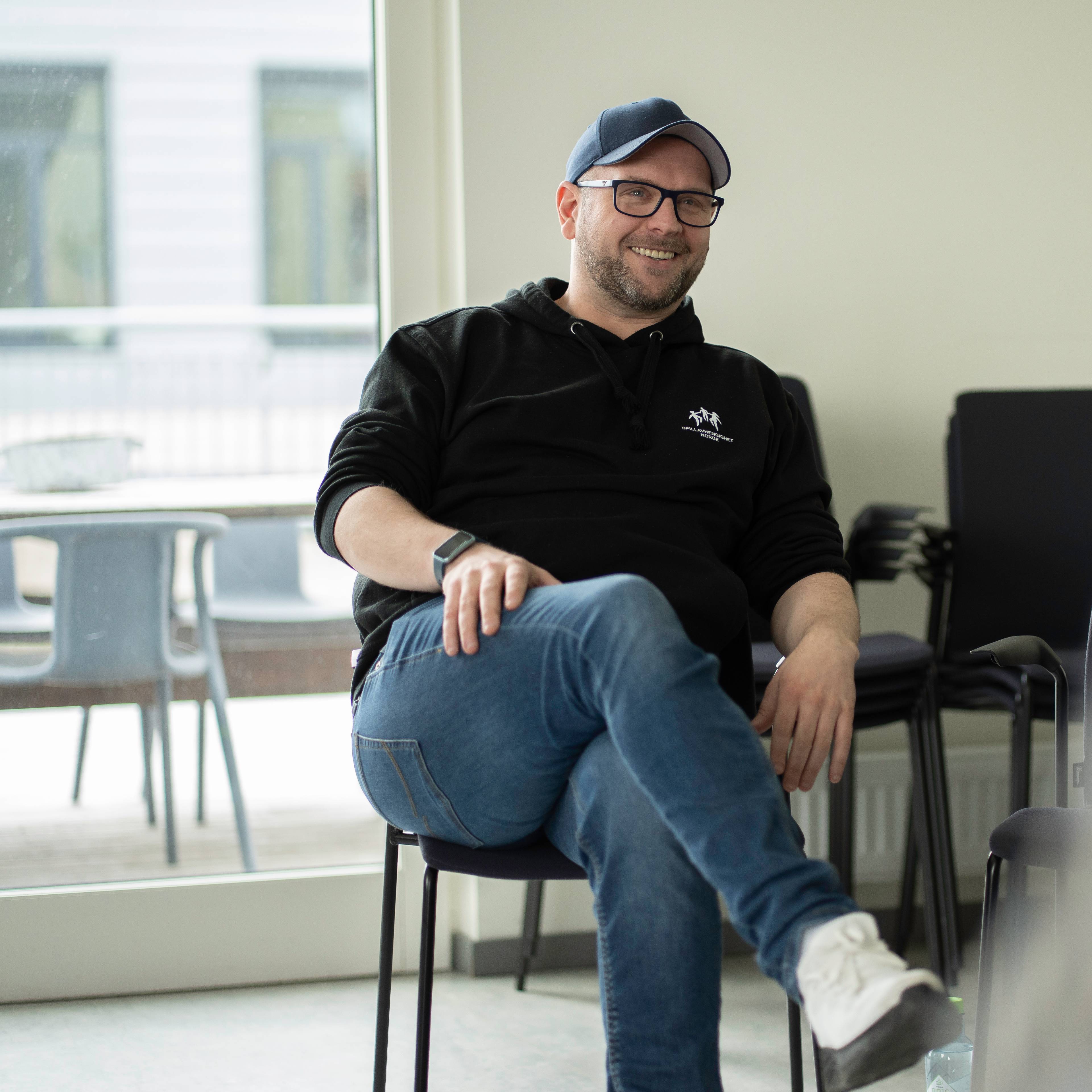 Mann sitter  på stol og smiler