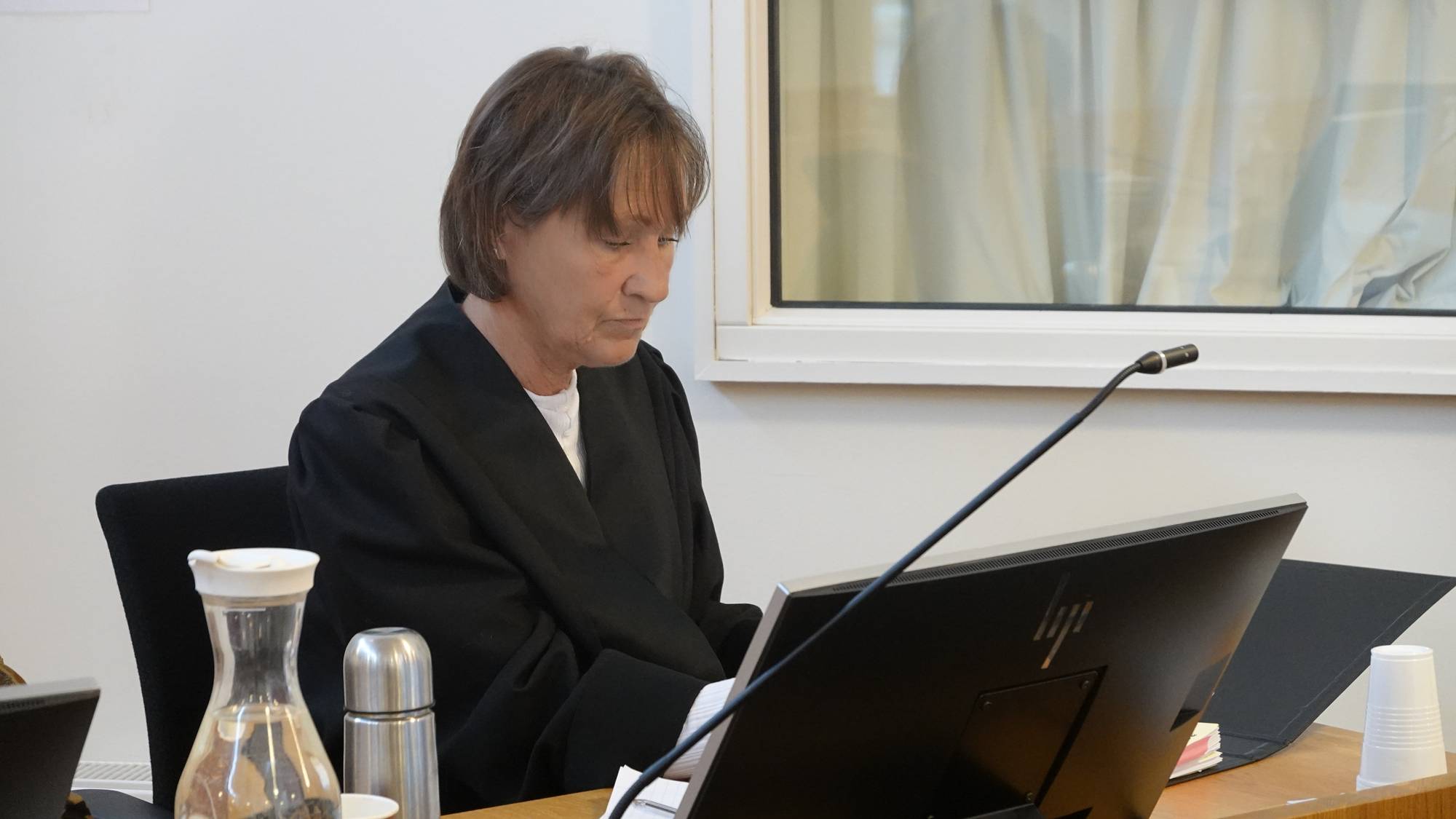 En dommer sitter ved et skrivebord i en rettssal og ser ned på en dataskjerm. (Bildebeskrivelsen er laget av en KI-tjeneste)