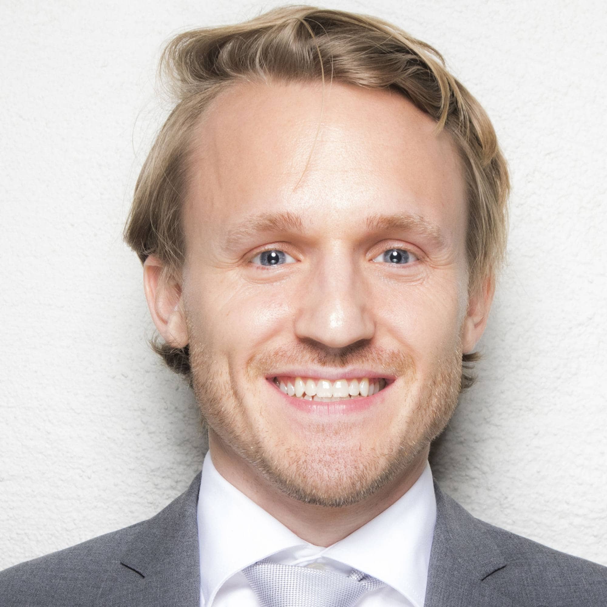 Portrett av en lyshåret mann i dress og slips mot en lys bakgrunn. (Bildebeskrivelsen er laget av en KI-tjeneste)