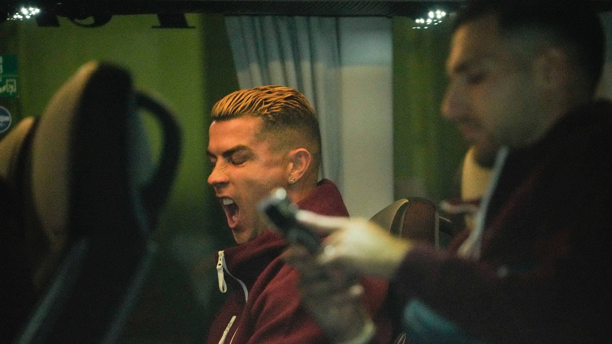 Cristiano Ronaldo gjesper mens han sitter på en buss. En annen person sitter i forgrunnen. (Bildebeskrivelsen er laget av en KI-tjeneste)
