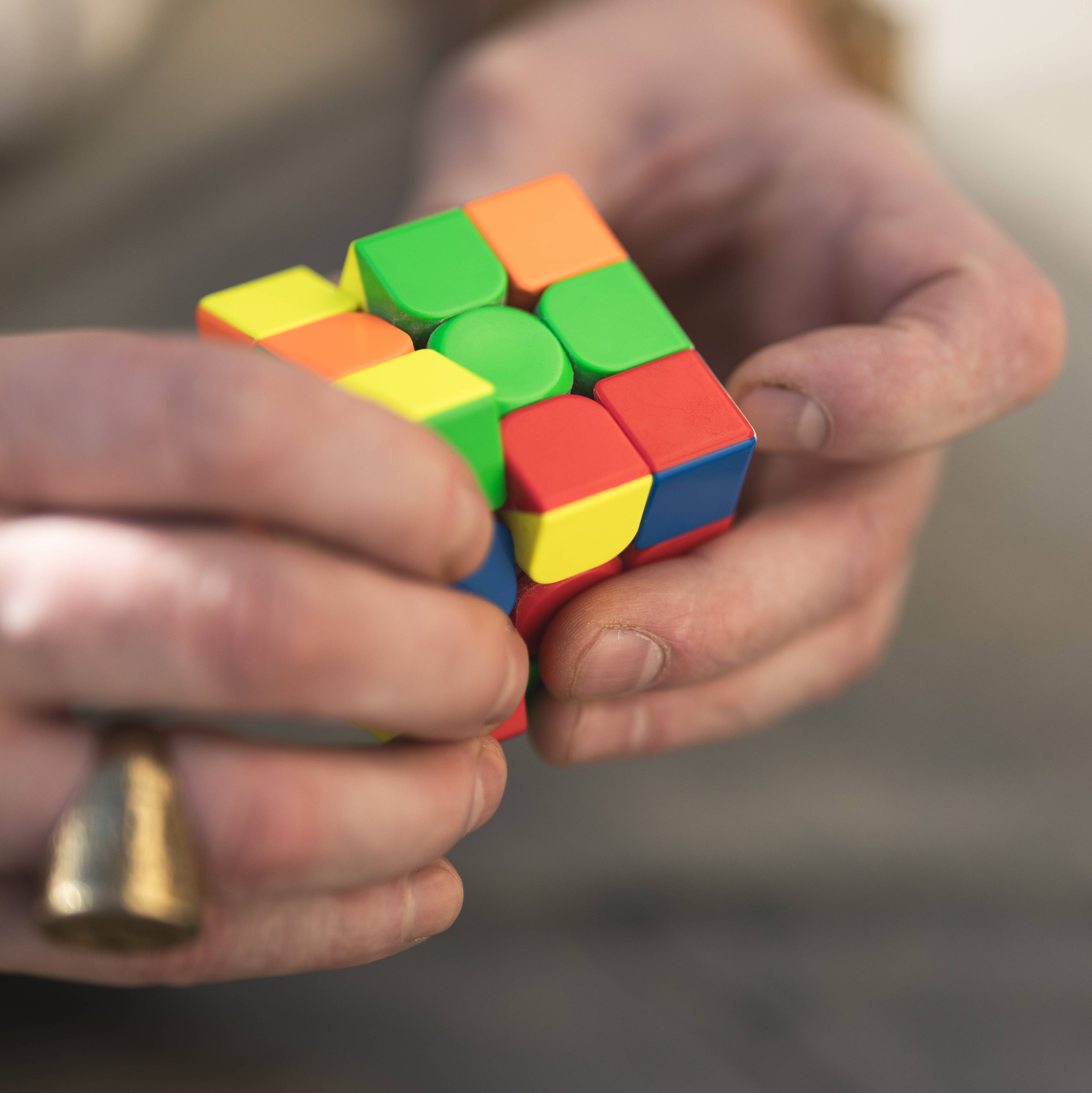 Mannshender som holder på med en Rubiks kube.