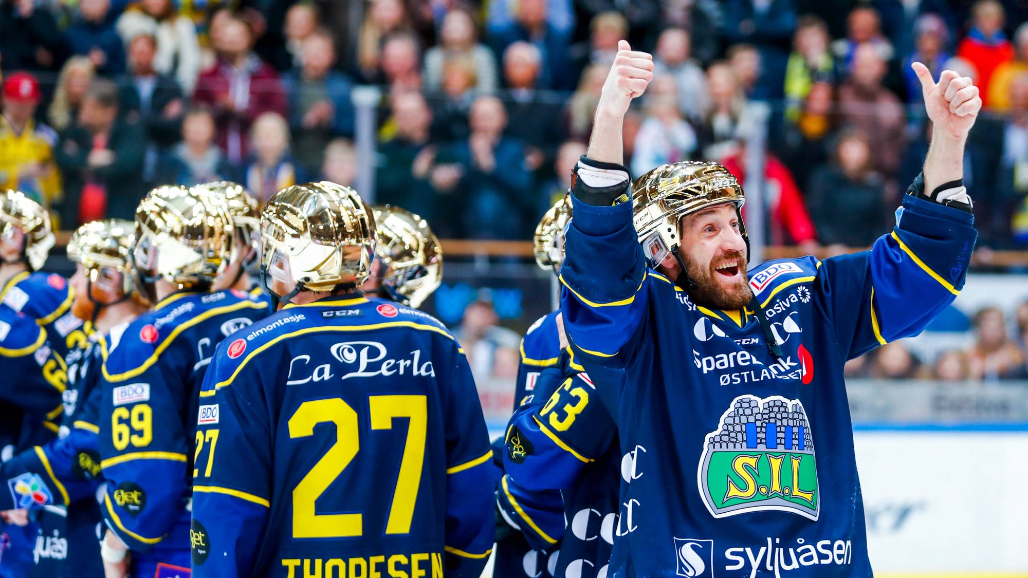 Ishockeyspiller jubler med hevede tomler foran lagkamerater i en arena. (Bildebeskrivelsen er laget av en KI-tjeneste)