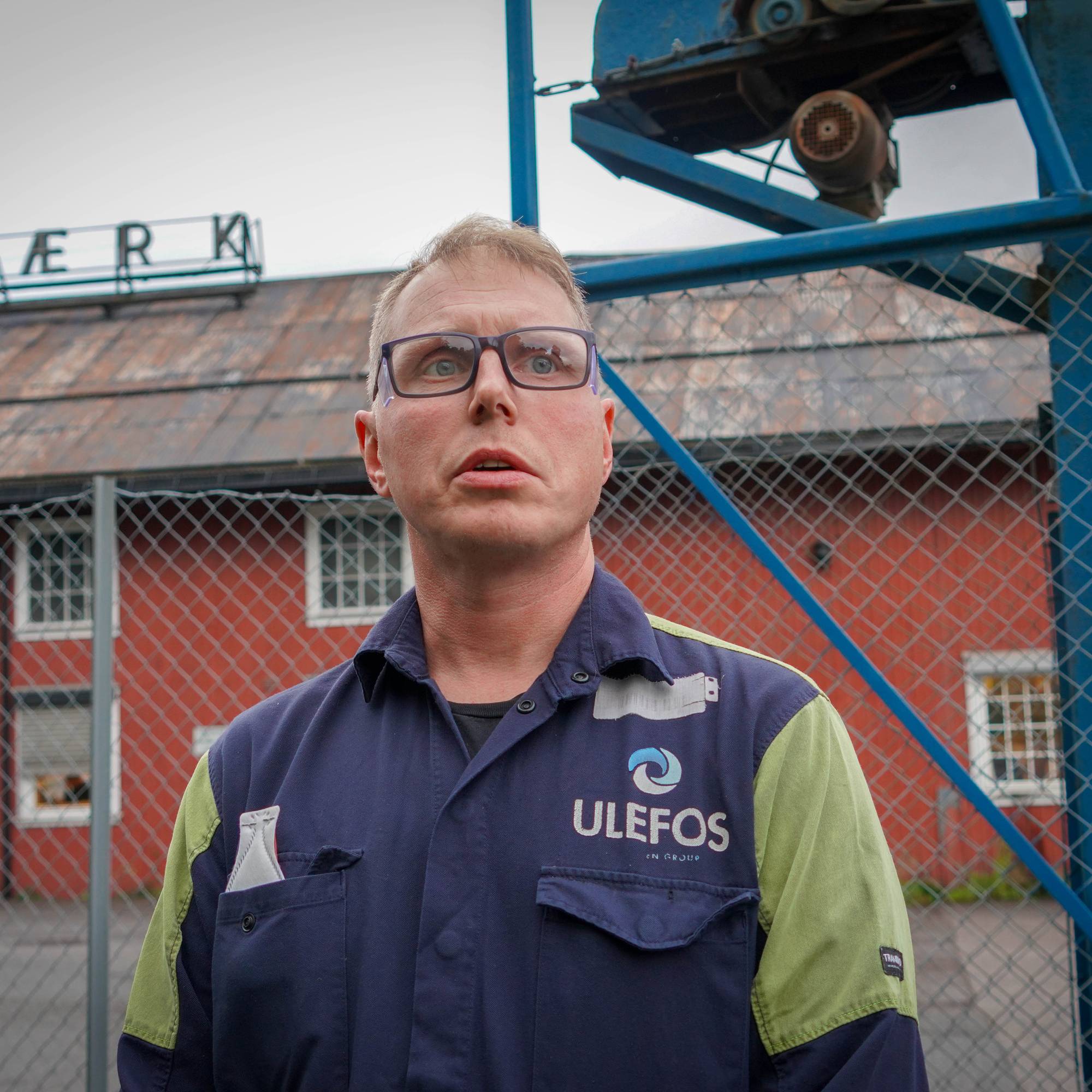 Mann i arbeidsuniform fra Ulefos foran en rød fabrikkbygning. (Bildebeskrivelsen er laget av en KI-tjeneste)