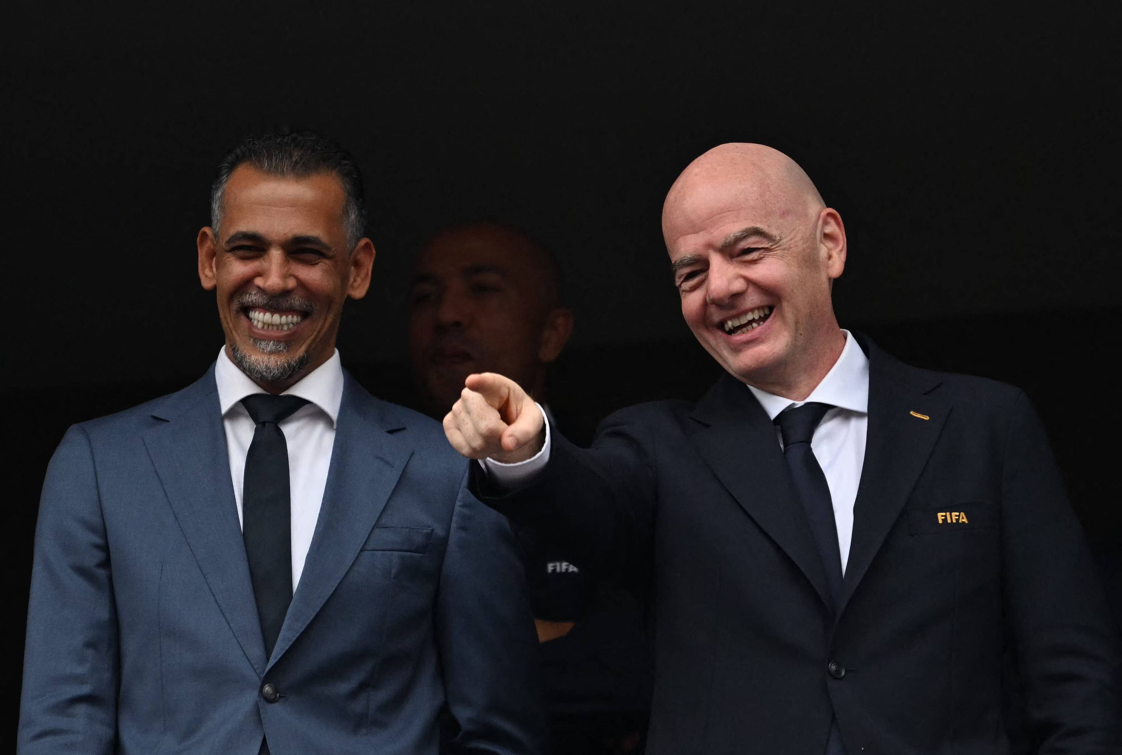 FIFA-president Gianni Infantino peiker og smiler saman med ein mann i dress. (Bildebeskrivelsen er laget av ein KI-teneste)