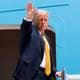AP Donald Trump vinker fra et flys trapp. Han er kledd i en mørk dress og en gul slip. Trump står ved inngangen til et lyseblått fly. (Bildebeskrivelsen er laget av en KI-tjeneste)