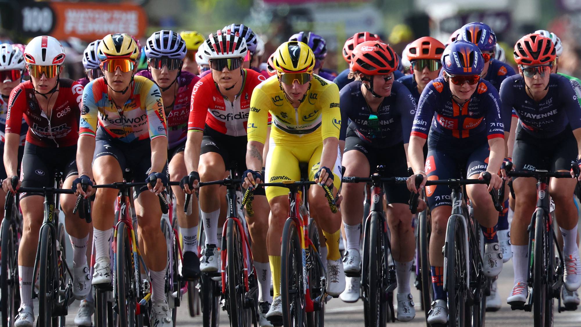 En gruppe syklister i Tour de France Femmes sykler samlet på en vei. Syklisten i gul trøye leder. (Bildebeskrivelsen er laget av en KI-tjeneste)