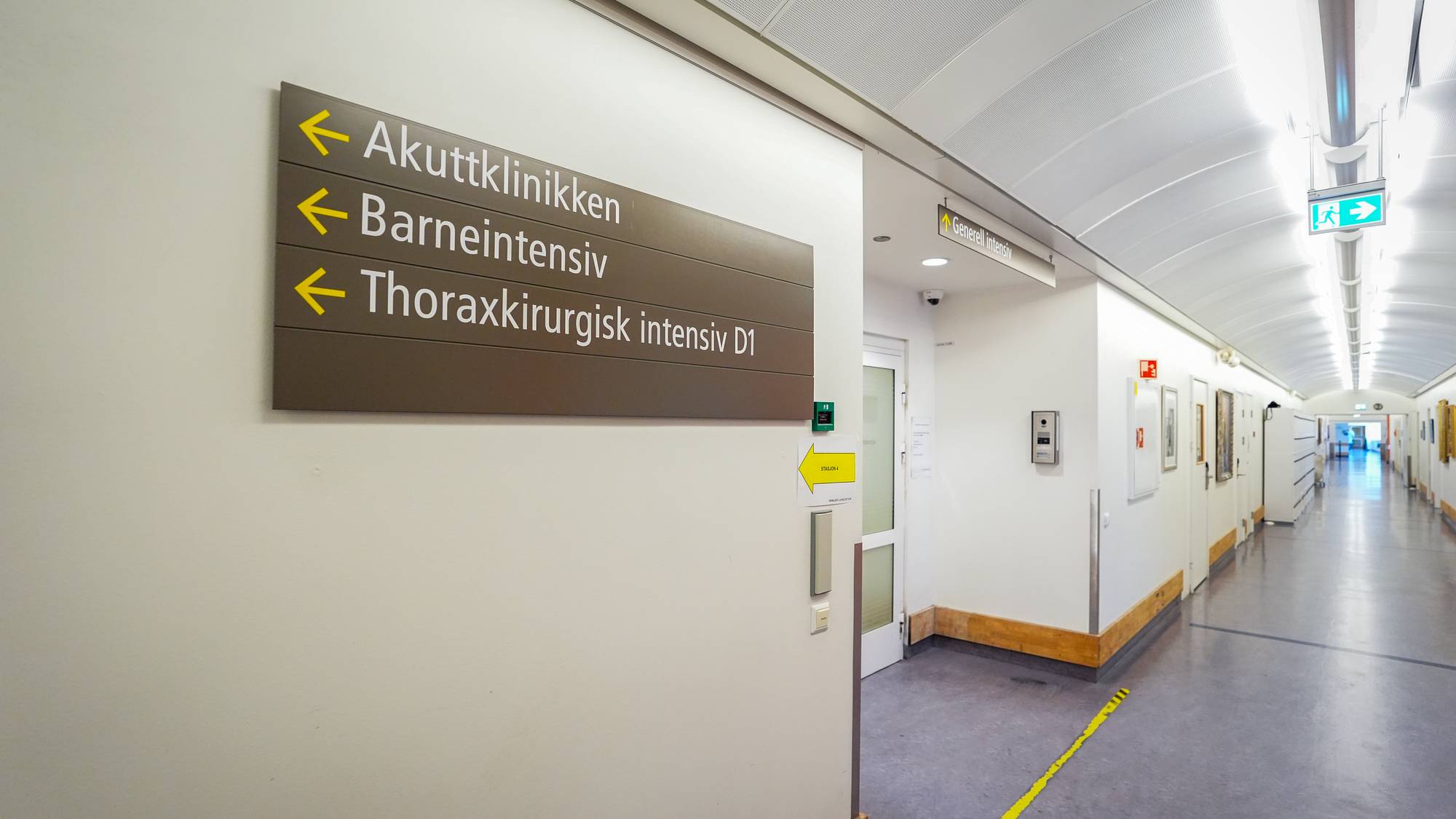 Skilt viser veien til Akuttklinikken, Barneintensiv og Thoraxkirurgisk intensiv D1. Et skilt med "Generell intensiv" henger lenger inne i korridoren. En grønn nødutgangsskilt er synlig. Korridoren er lys og hvit med et buet tak. (Bildebeskrivelsen er laget av en KI-tjeneste)