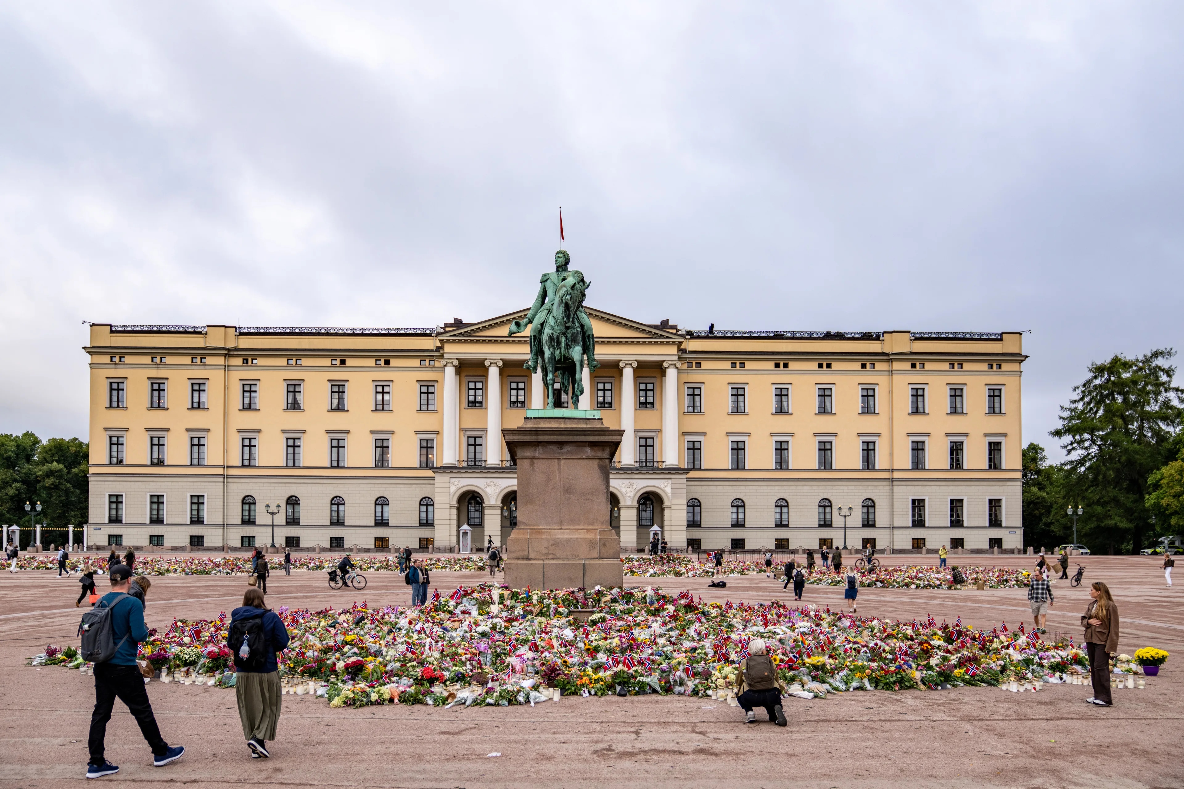 Folk legger ned blomster ved rytterstatuen framfor Det kongelege slott i Oslo. (Bildebeskrivelsen er laget av en KI-teneste)