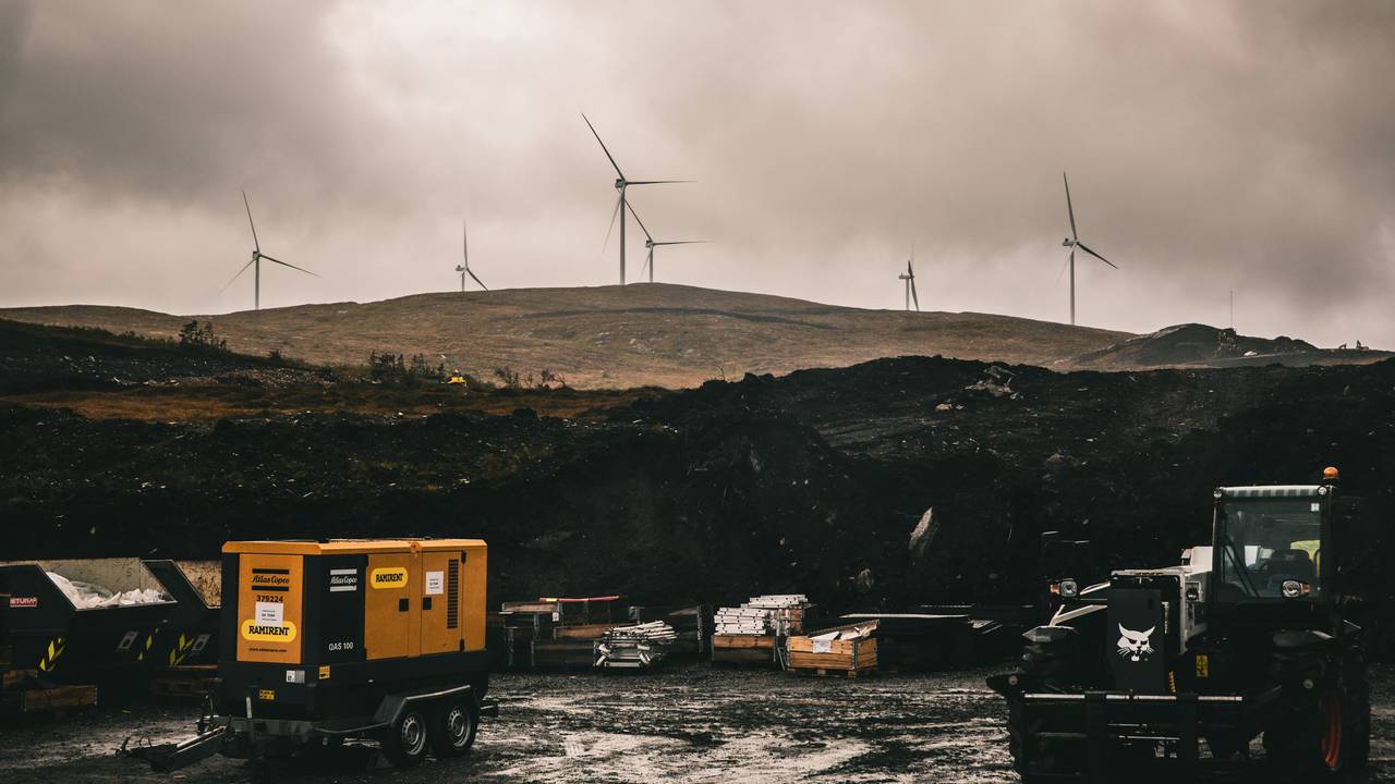 Et ultratotalt utsnitt av Geitfjellet vindkraftverk på Fosen i Trøndelag. I forgrunnen ser man en anleggplass med ulike maskiner. I bakgrunnen skimtes flere vindturbiner og en mørk himmel.