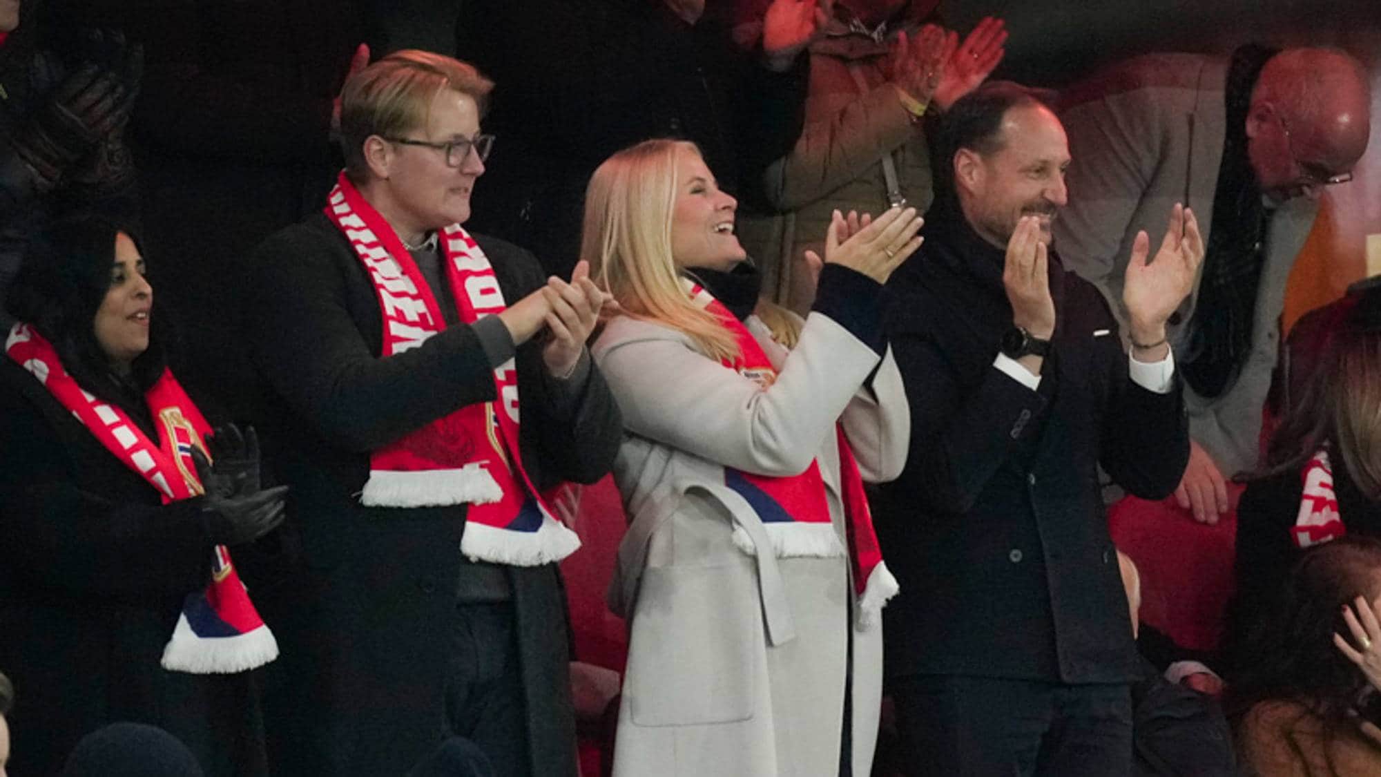 Kronprins Haakon og kronprinsesse Mette-Marit applauderer på tribunen med norske supportere. (Bildebeskrivelsen er laget av en KI-tjeneste)