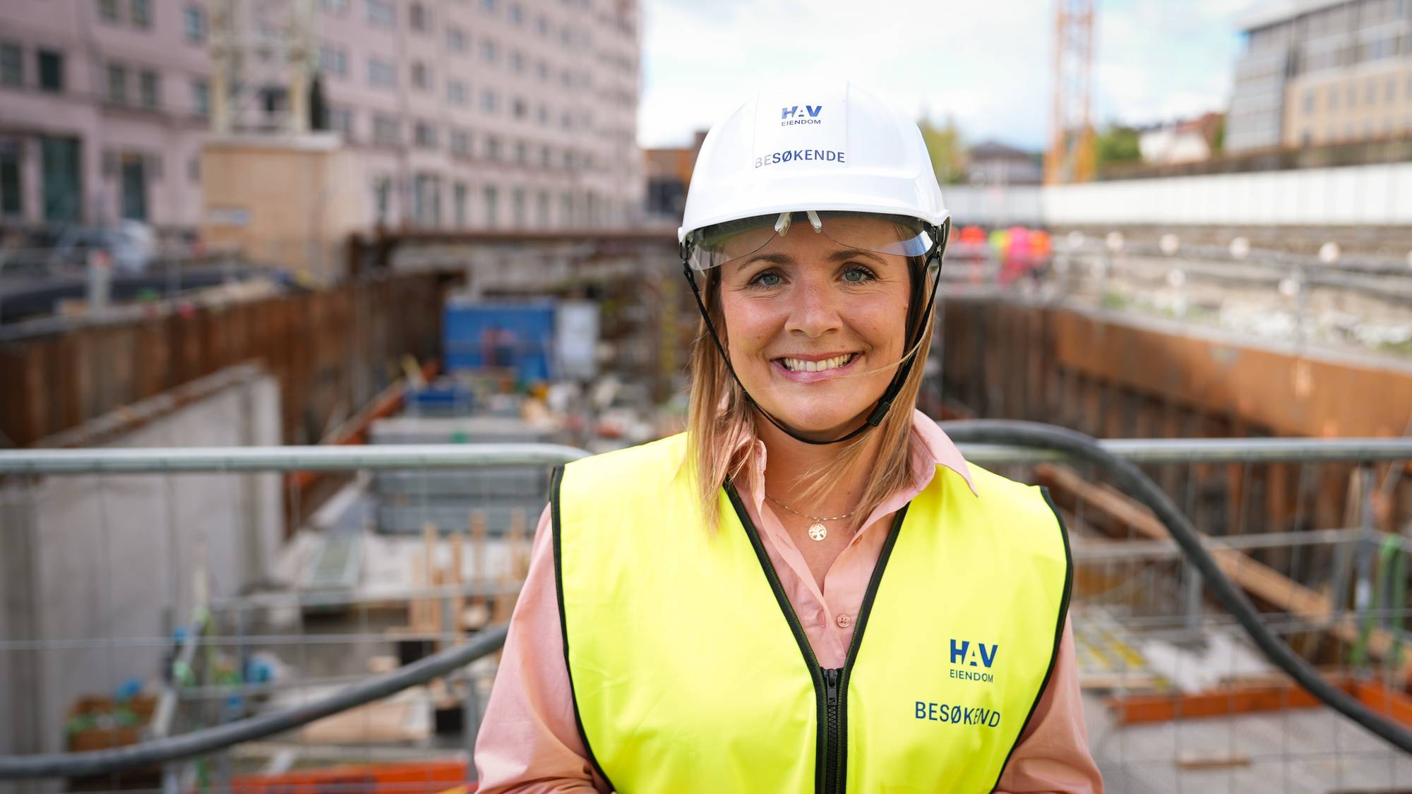 Kvinne med vernehjelm og refleksvest på en byggeplass. 