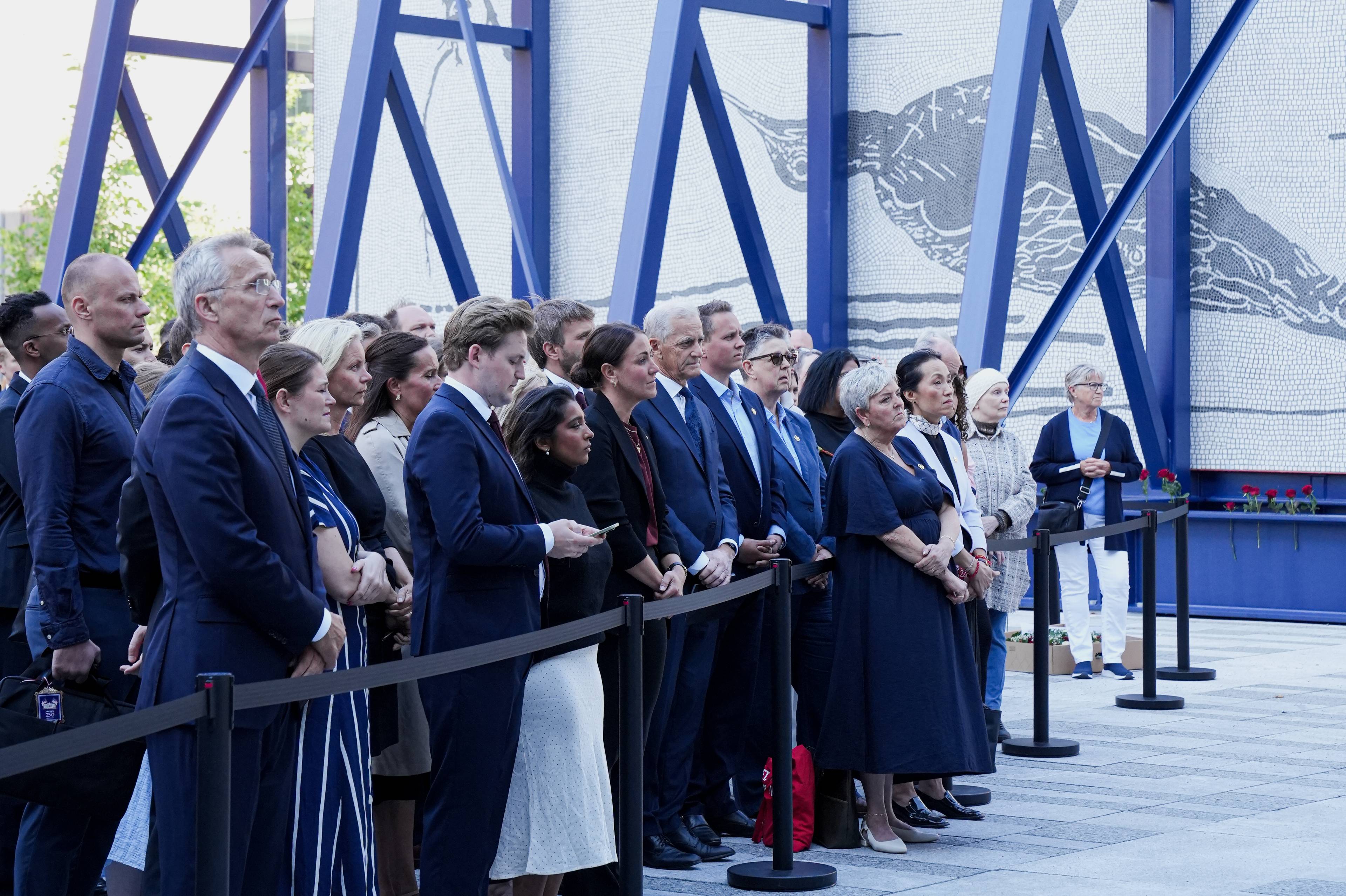 Jens Stoltenberg, Tonje Brenna, Jonas Gahr Støre og flere står utendørs foran 22. juli-minnesmerket ved Regjeringskvartalet