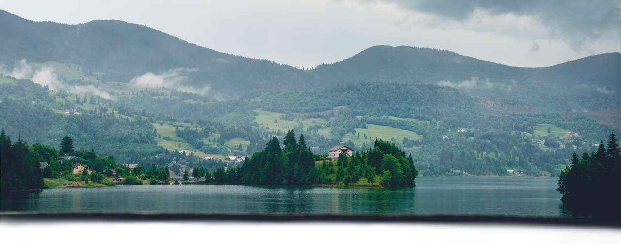 Lake immersed in the green of the mountains with an island with a house in the center.