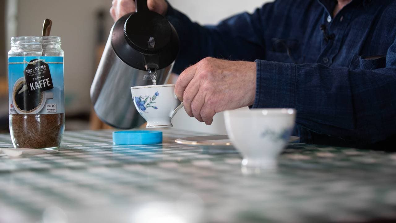 Varmt vann renner fra en kanne ned i en kaffeekopp med blå blomster