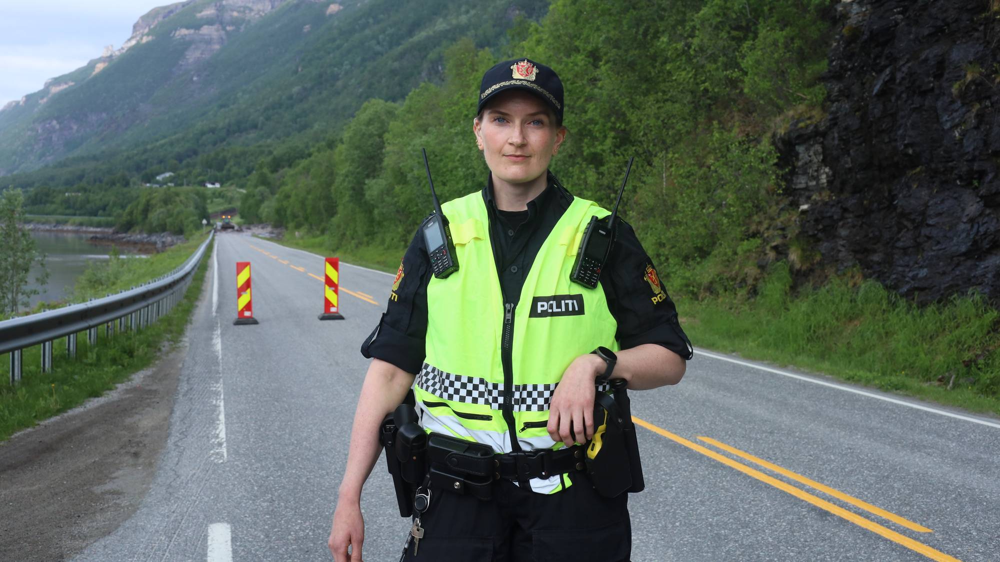 en kvinnelig politibetjent står på en vei med sperringer i bakgrunnen