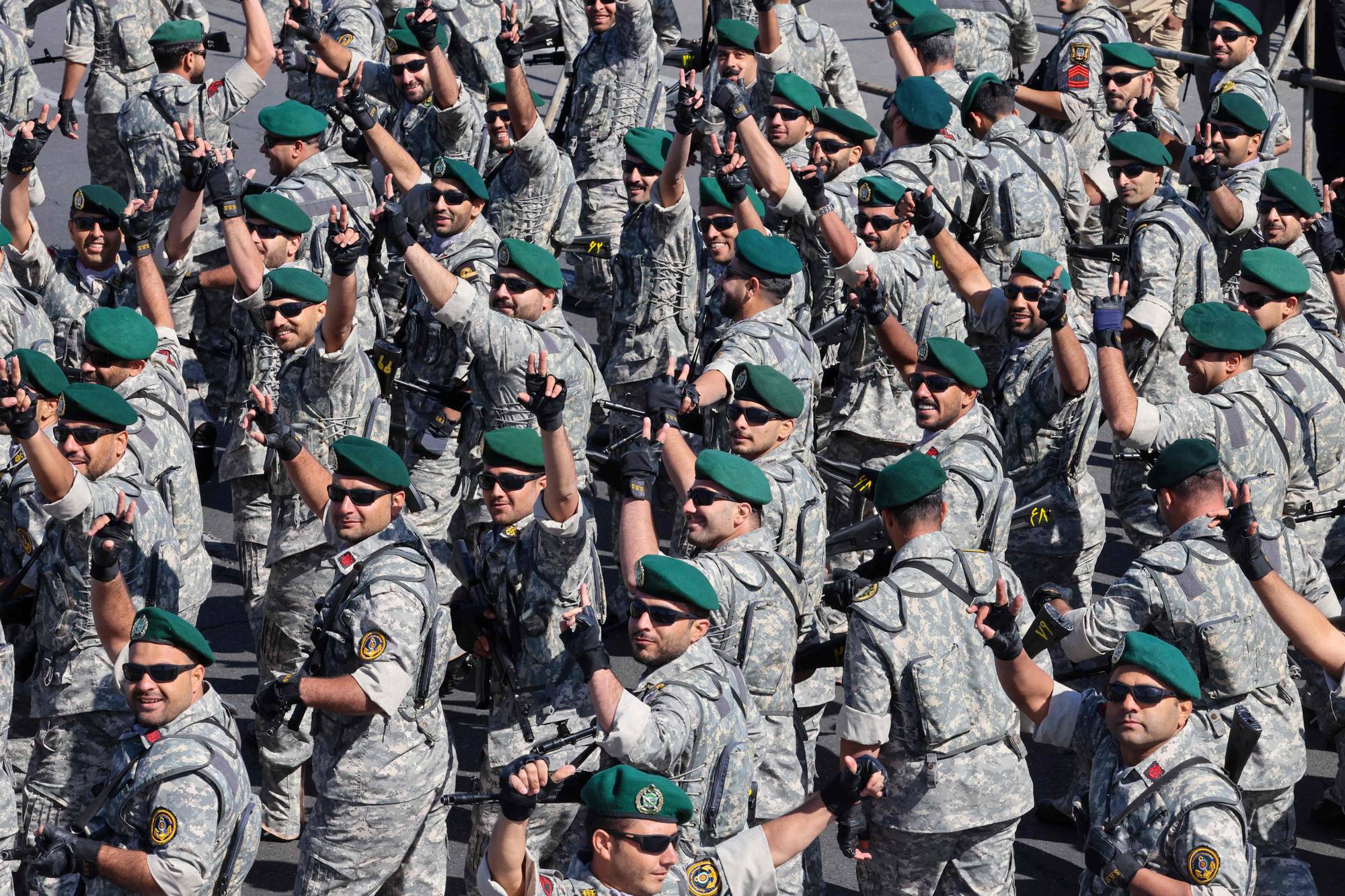 Militære menn med grønne bereter og kamuflasjedrakter marsjerer. De vinker og holder opp to fingre. Mange av dem har solbriller. Bildet viser en stor gruppe soldater i en parade. (Bildebeskrivelsen er laget av en KI-tjeneste)