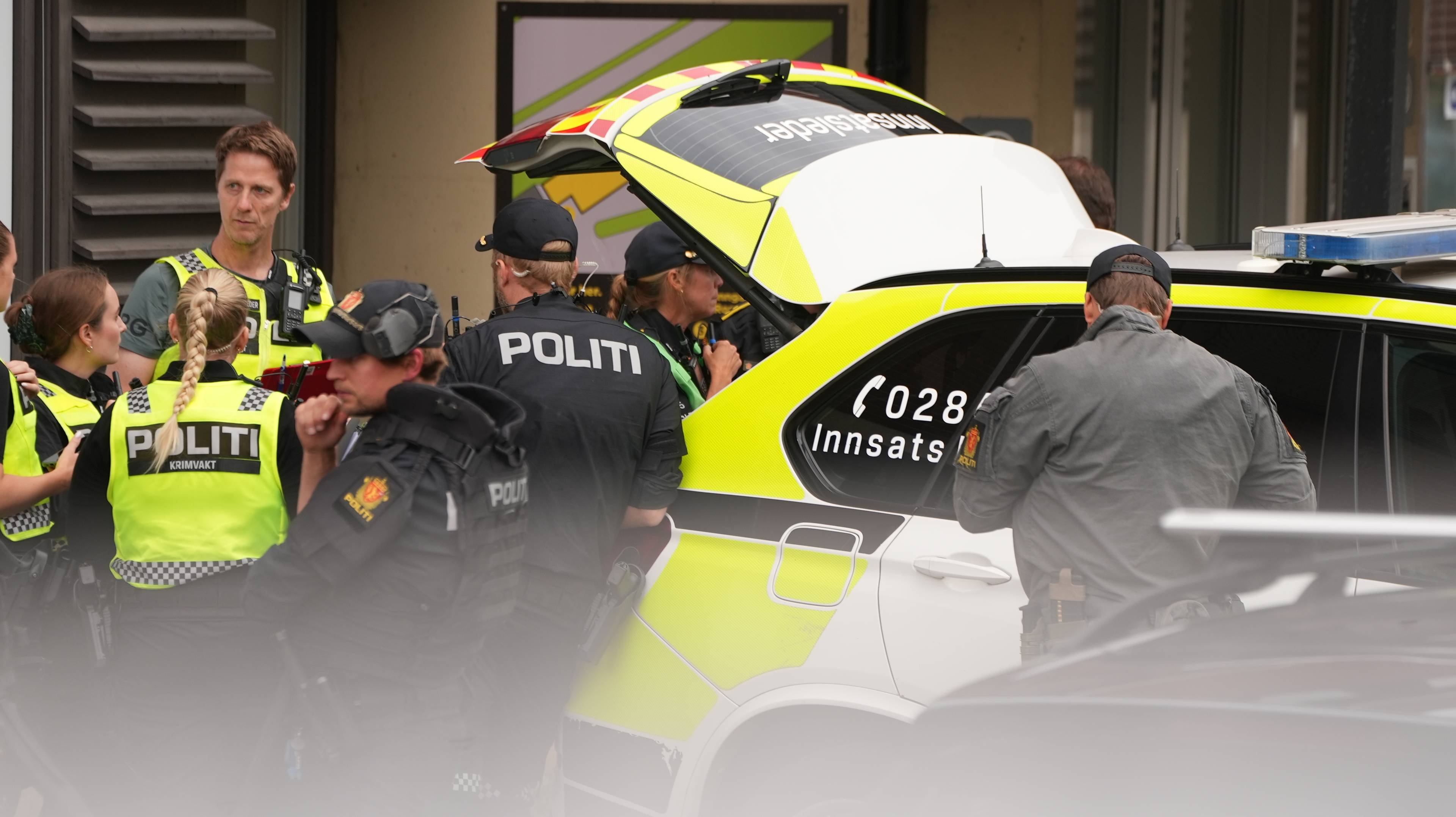 Politi ved en innsatsbil med åpent bagasjerom utendørs. (Bildebeskrivelsen er laget av en KI-tjeneste)