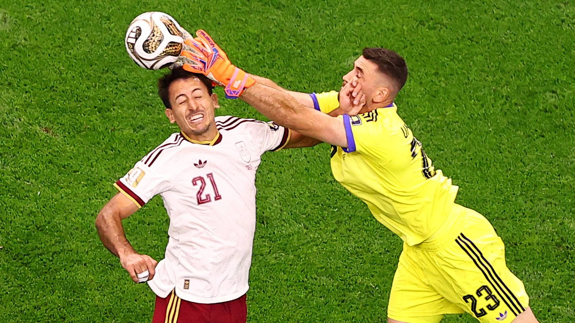 En keeper i gul drakt bokser ballen vekk foran en motspiller i hvit drakt under en fotballkamp. (Bildebeskrivelsen er laget av en KI-tjeneste)