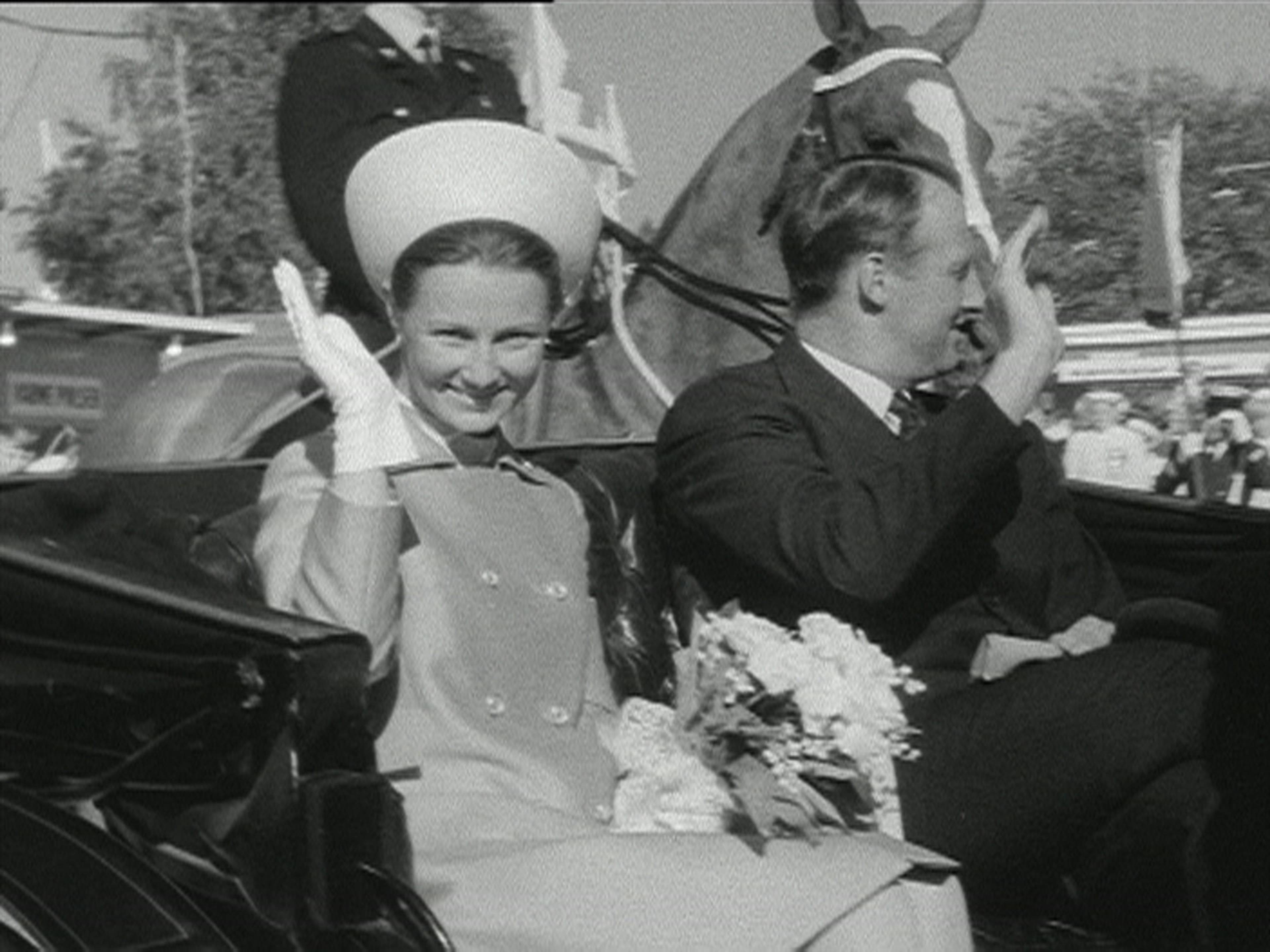 Kong Harald og dronning Sonja vinker fra en hestetrukket vogn.
