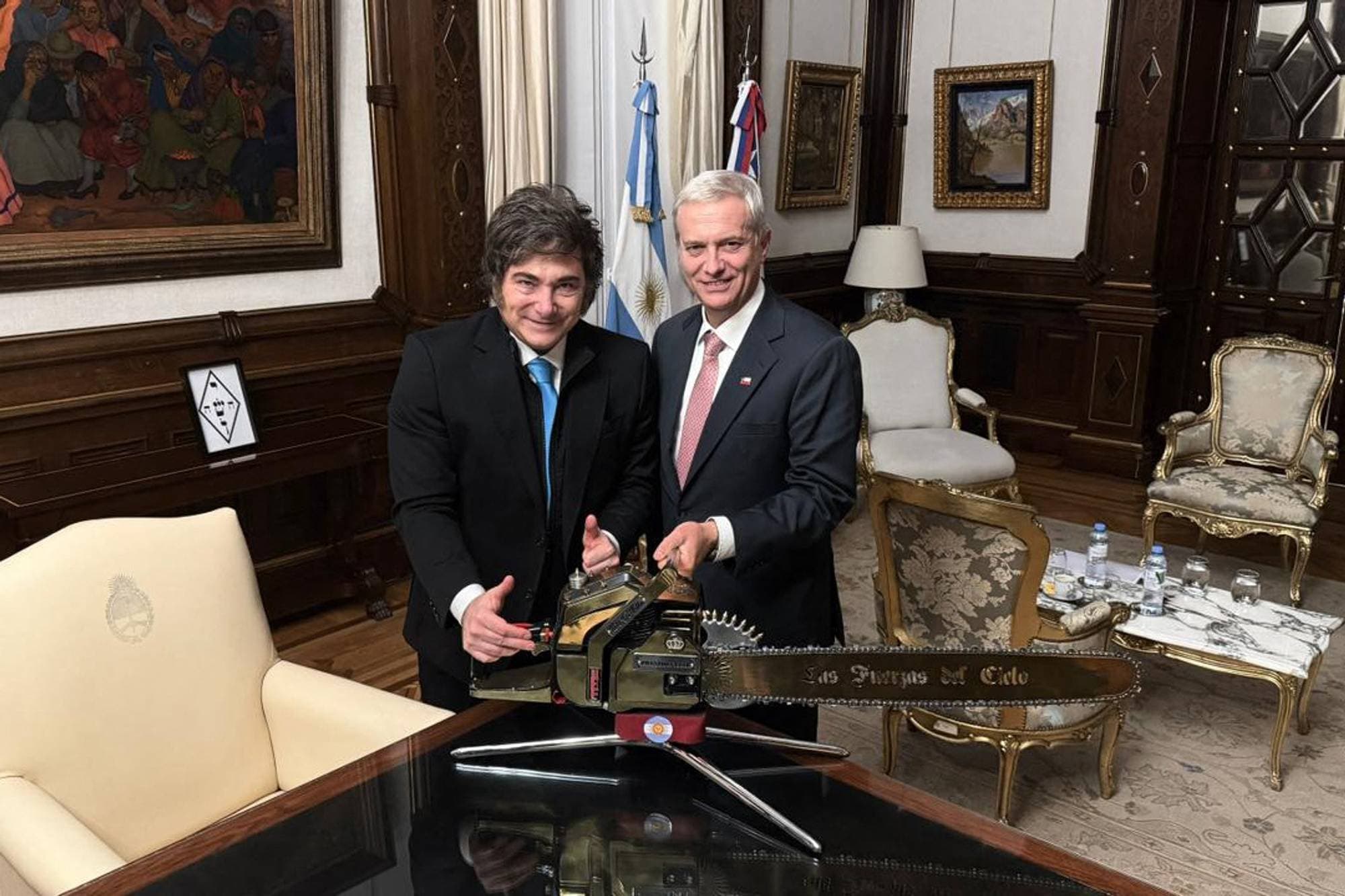 Argentinas president Javier Milei står med en motorsag sammen med en mann i et formelt rom. 