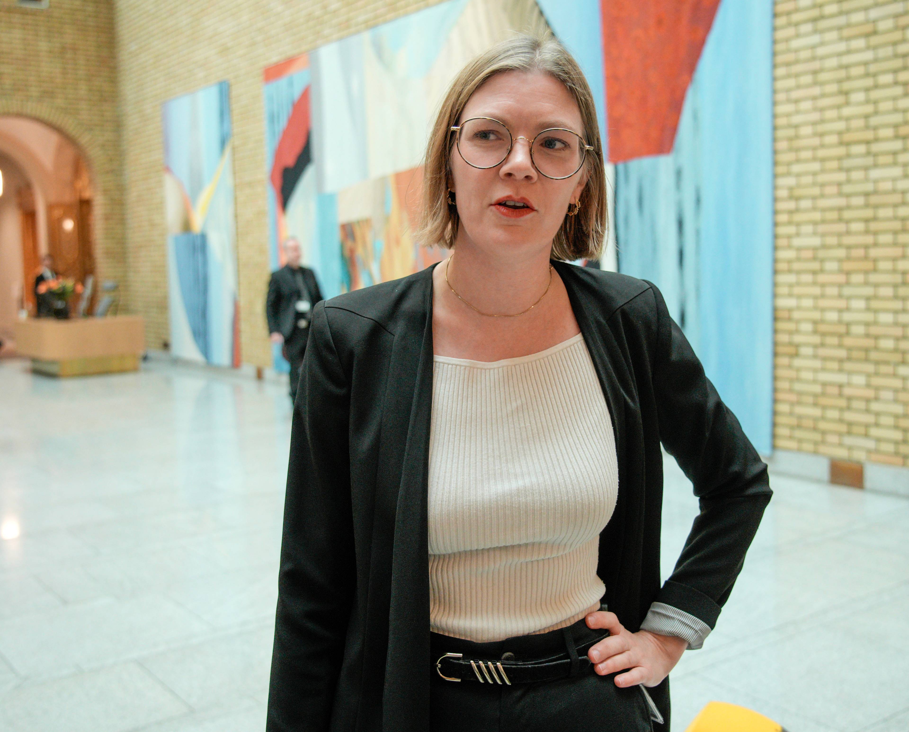Marie Sneve Martinussen (R) på Stortinget. Hun har på seg svart bukse, svart dressjakke og hvit t-skjorte. Hun har kort brunt hår og briller.