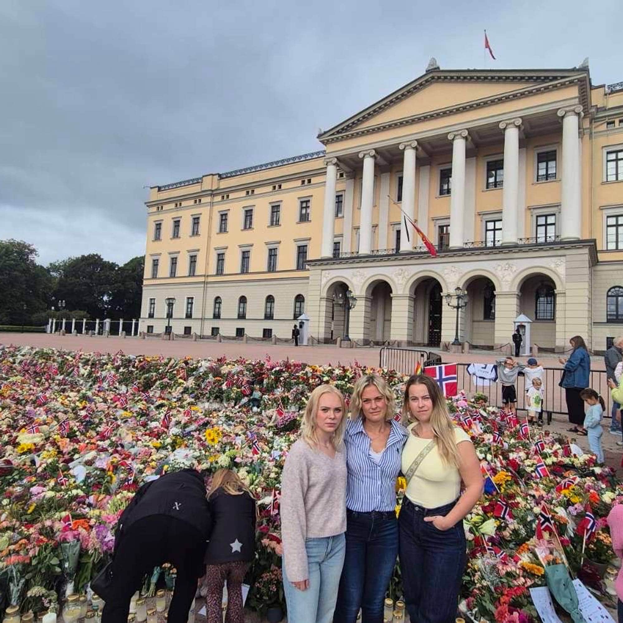 En kvinne står sammen med to jenter på slottsplassen med blomsterhavet i bakgrunnen.
